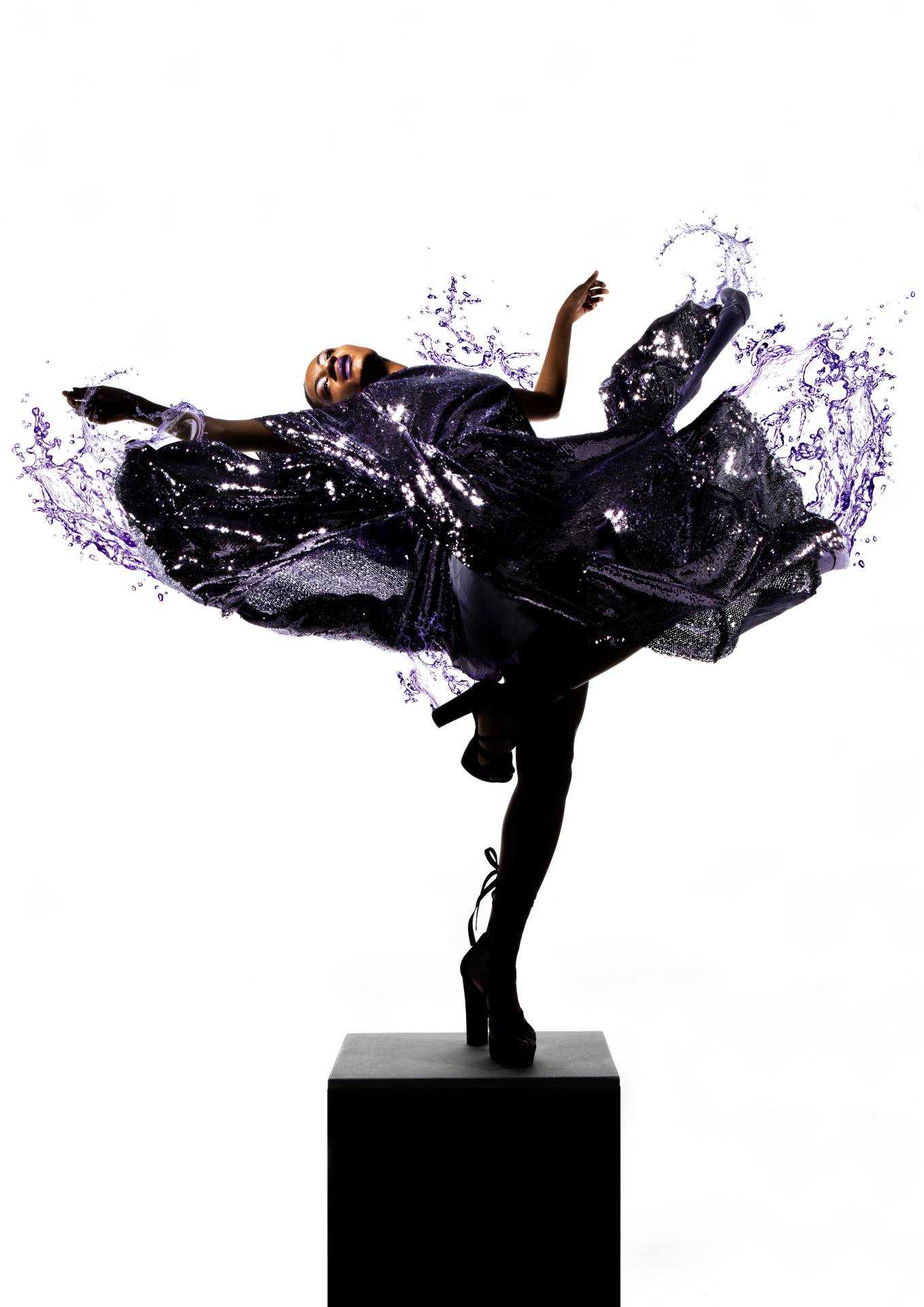 A model raises a leg up and leans backwards with their skirt flowing out around them. A liquid effect splashes out from the skirt.