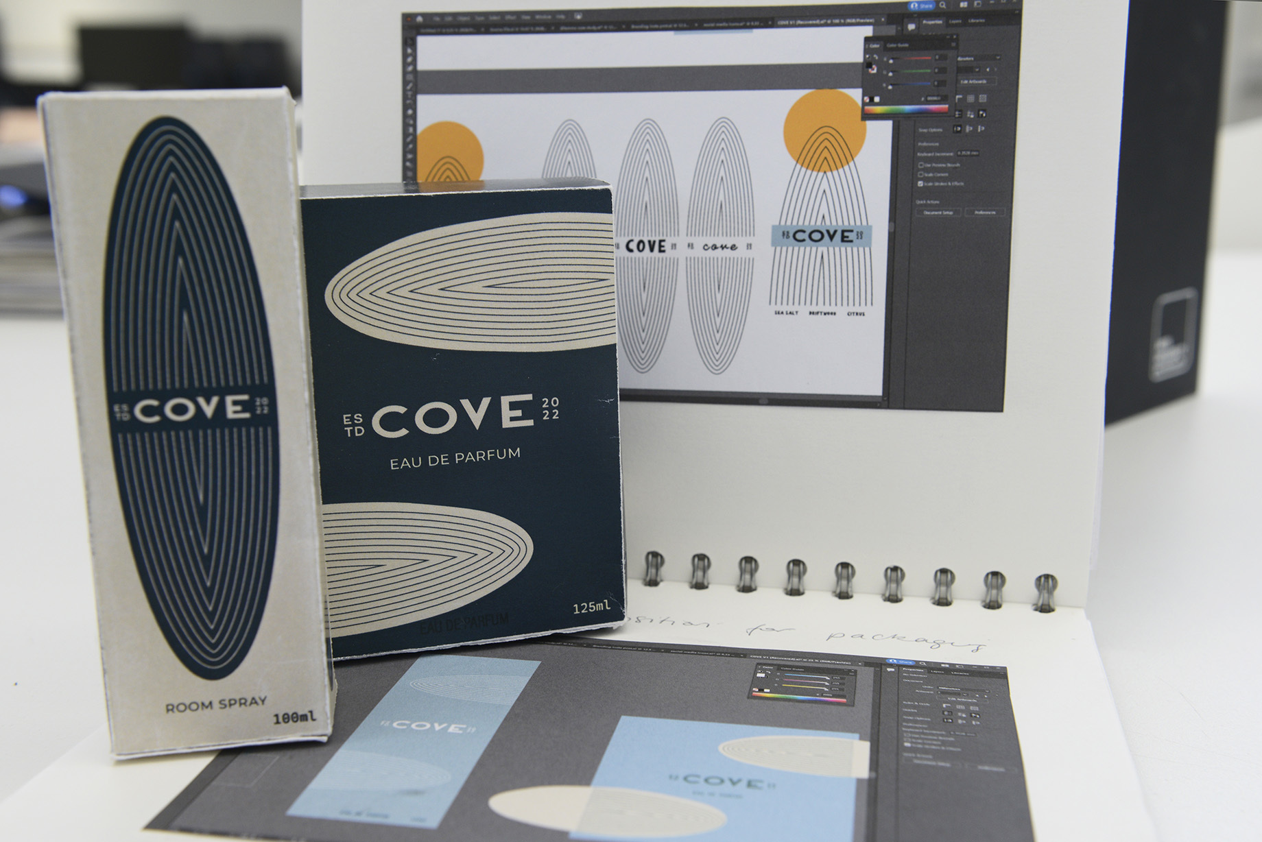 Two packaging boxes for a perfume called 'Cove', sitting on top of an open portfolio book.