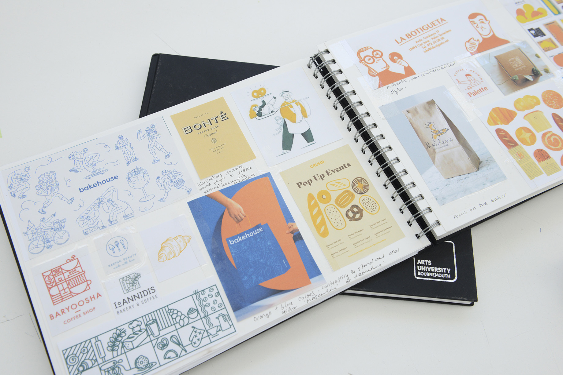 An open double-page spread of a portfolio book showing various designs and brand examples with handwritten notes.