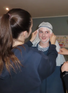 I am helping Becky get into her Edith costume by putting on her wimple as the finishing touch. This brings her character to life.