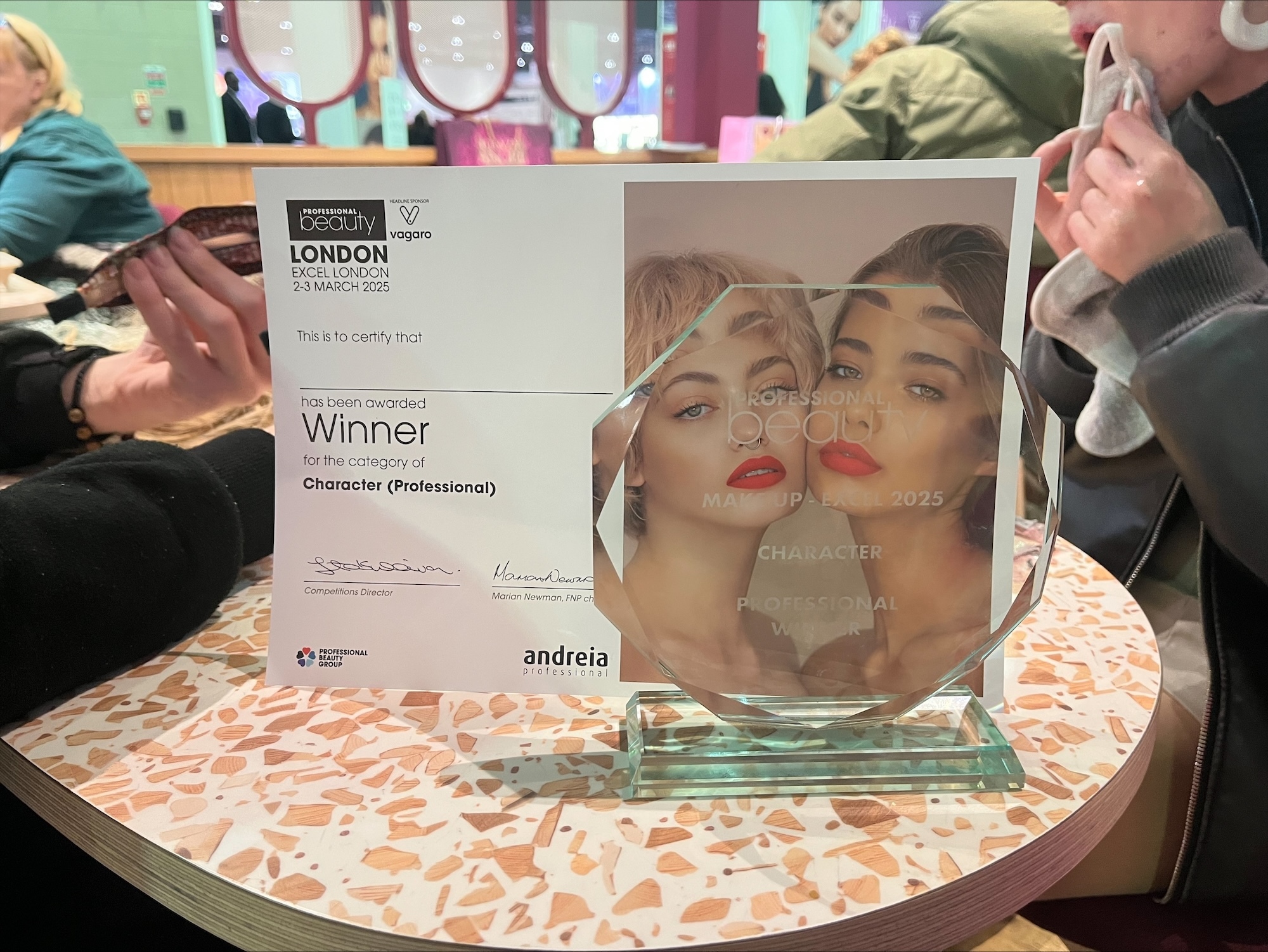 An octagonal glass award and a certificate behind it, for the Professional Beauty Make-up Competition 2025, displayed on a round table.