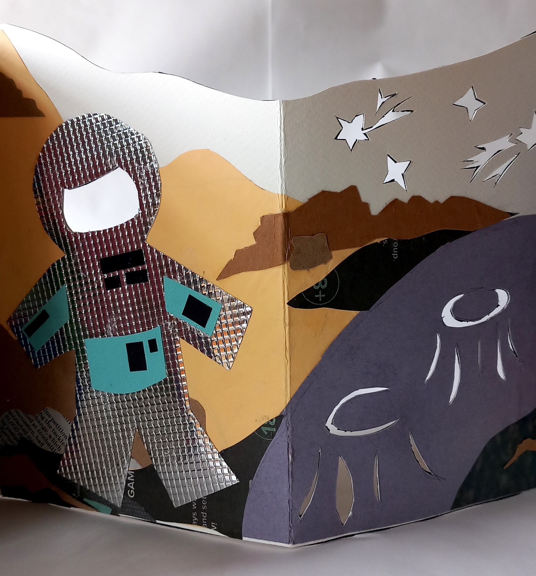 Open children's book showing astronaut figure in grey patterned suit with turquoise details on left page, purple planet with white crescent and stars on right page