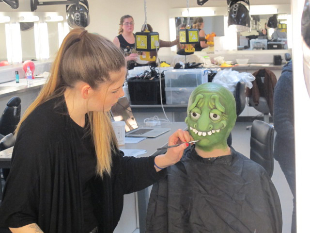 A student is painting another student's face with a green alien design.