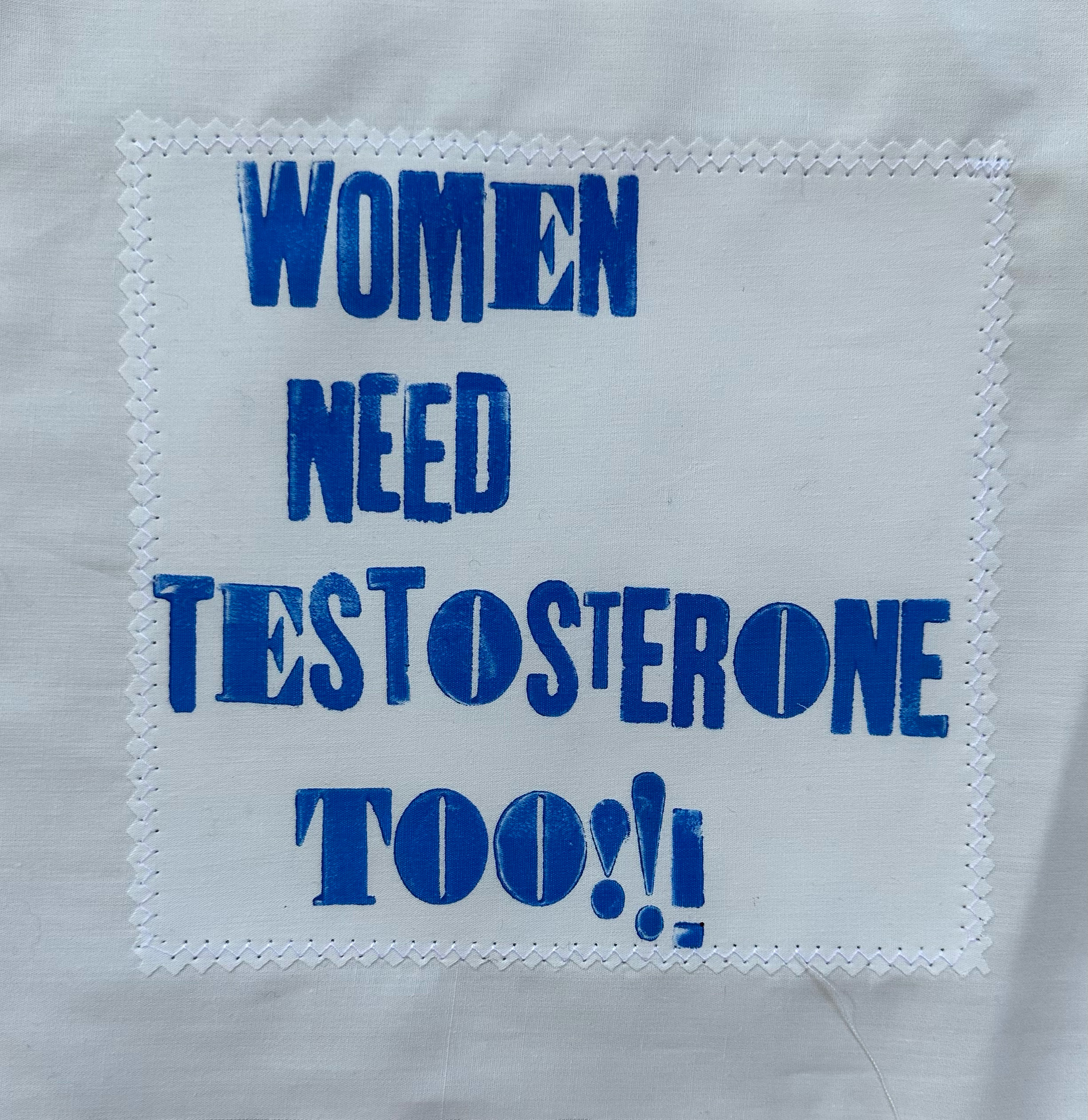 Blue text reading "WOMEN NEED TESTOSTERONE TOO!!" in capital letters within white dotted border on grey marble background.