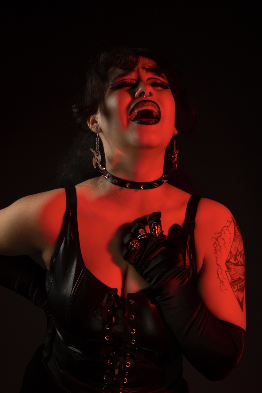 Kasandra Georgi in red lighting with black accessories posing emotionally.