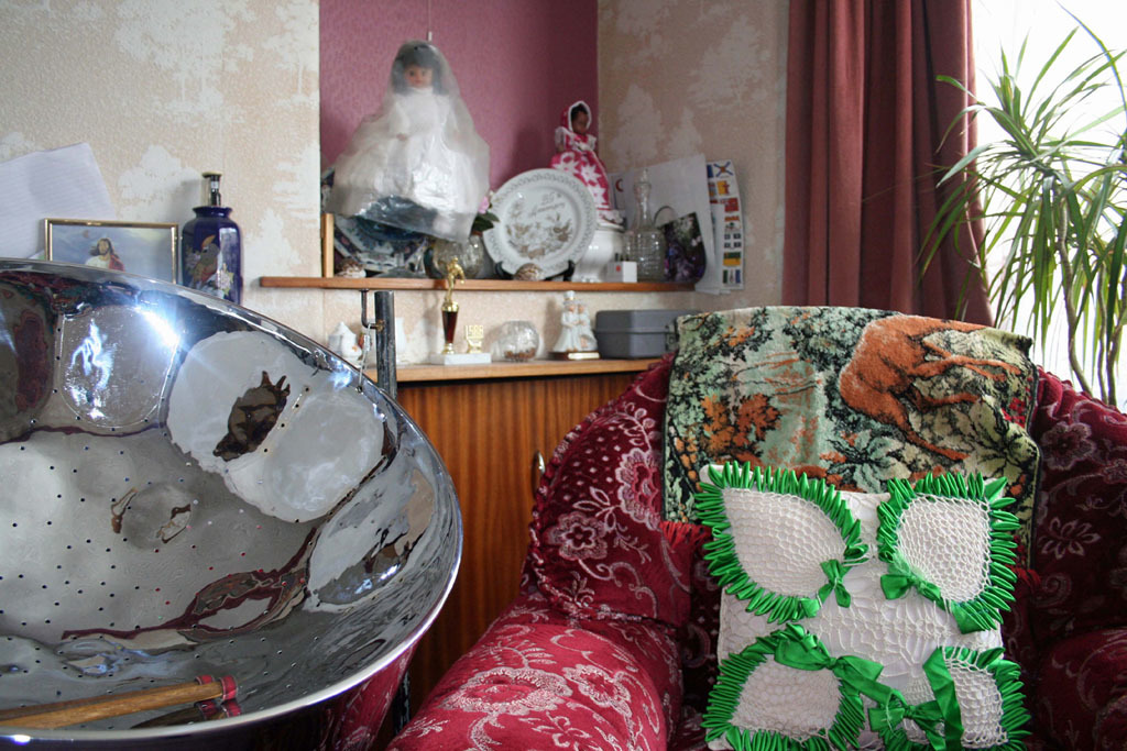 A large shiny strainer sits next to an armchair in a living room.