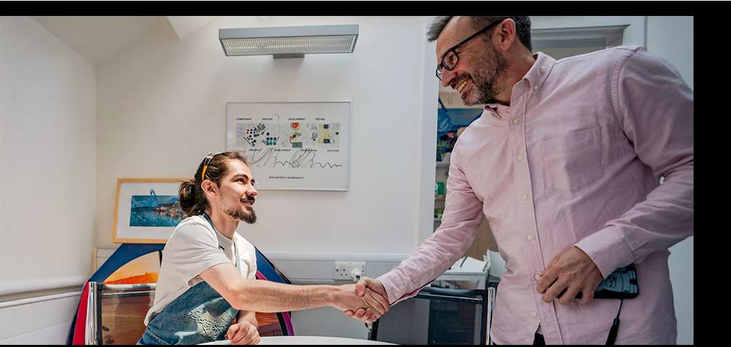 Two men shaking hands in modern office with white walls, colourful artwork, and contemporary furniture.