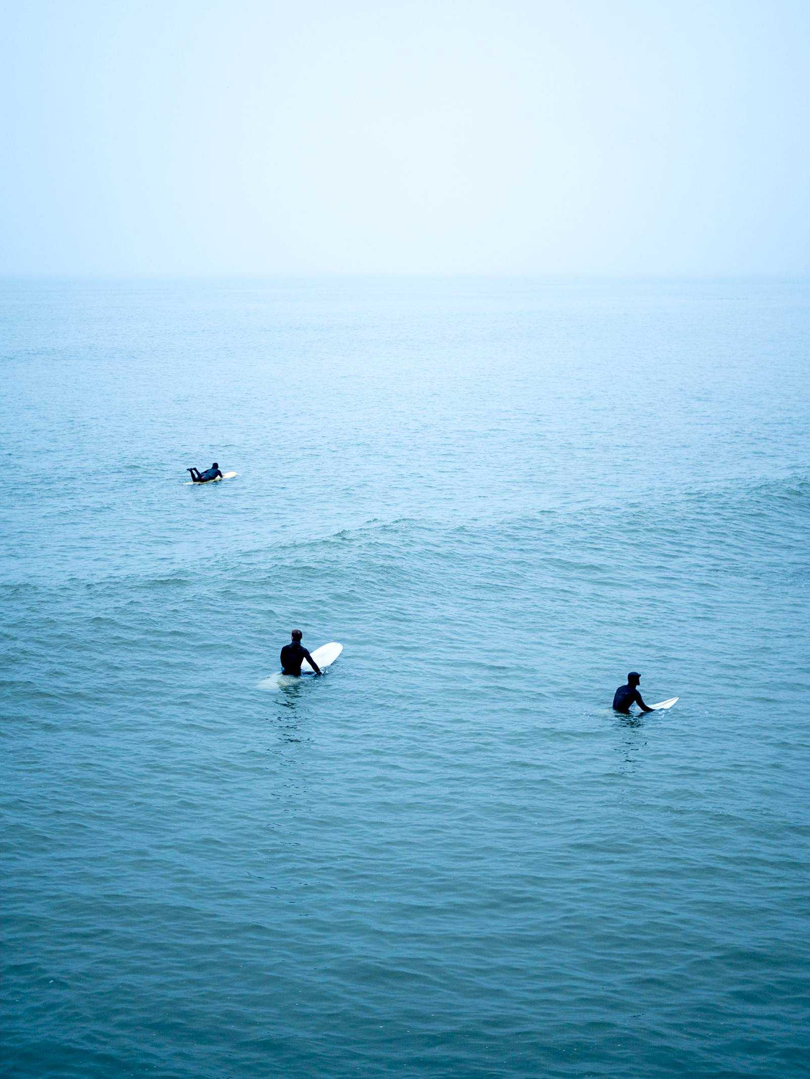 Three people on surfboards in the open sea.
