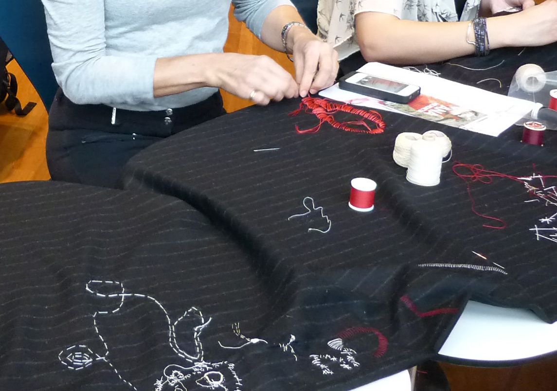 Hands working on a black pin-striped material. Red and white thread are being used