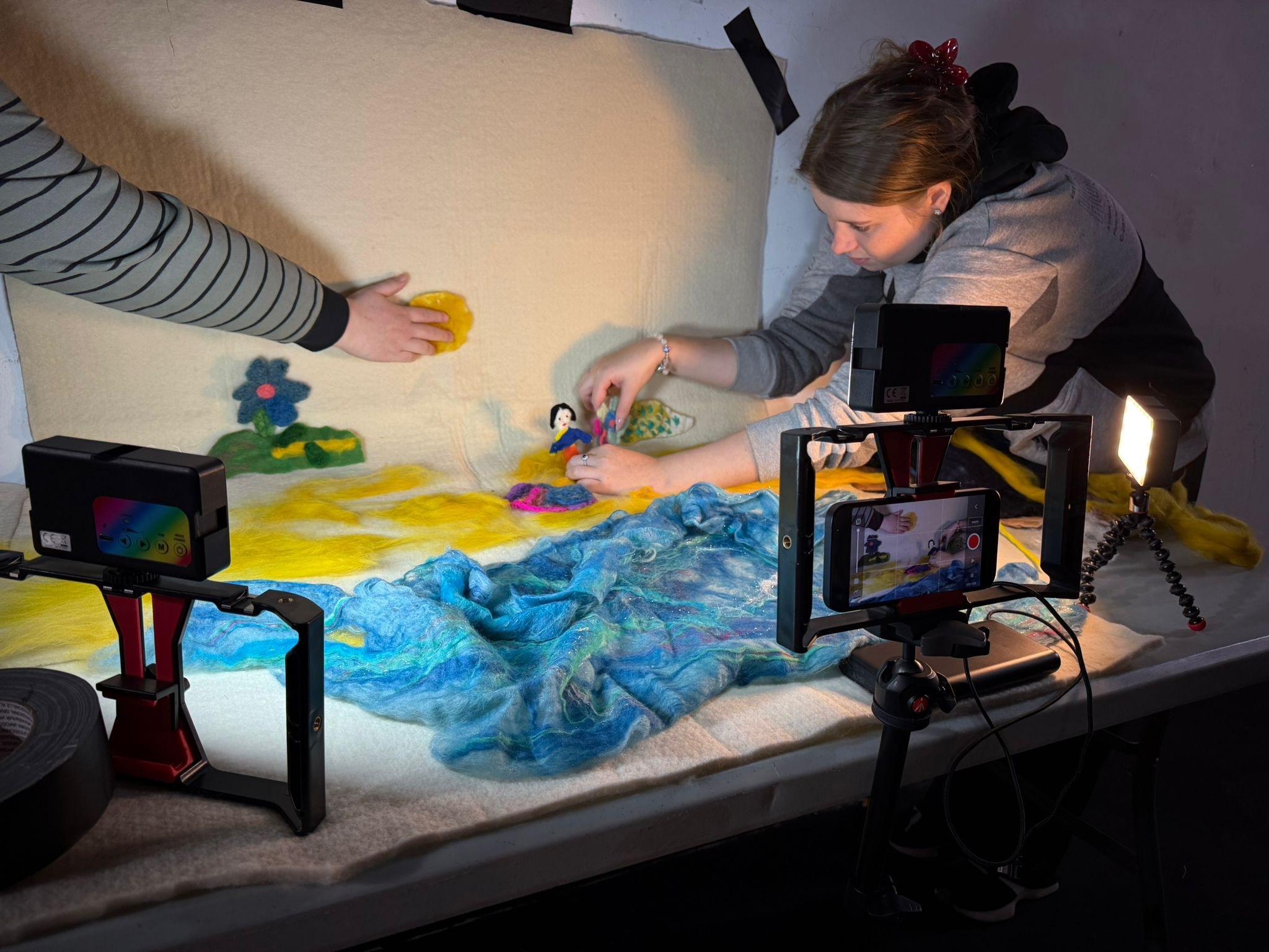 Woman leaning over light table creating colourful animation with blue and yellow materials, surrounded by cameras and equipment.