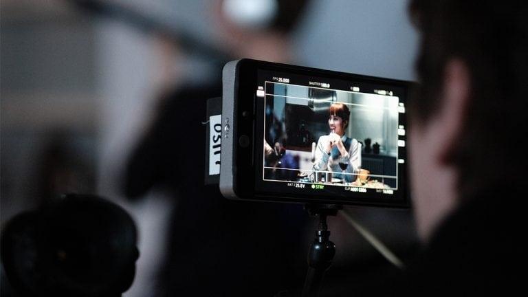 A woman sitting at a dinner table, viewed through a film camera monitor.