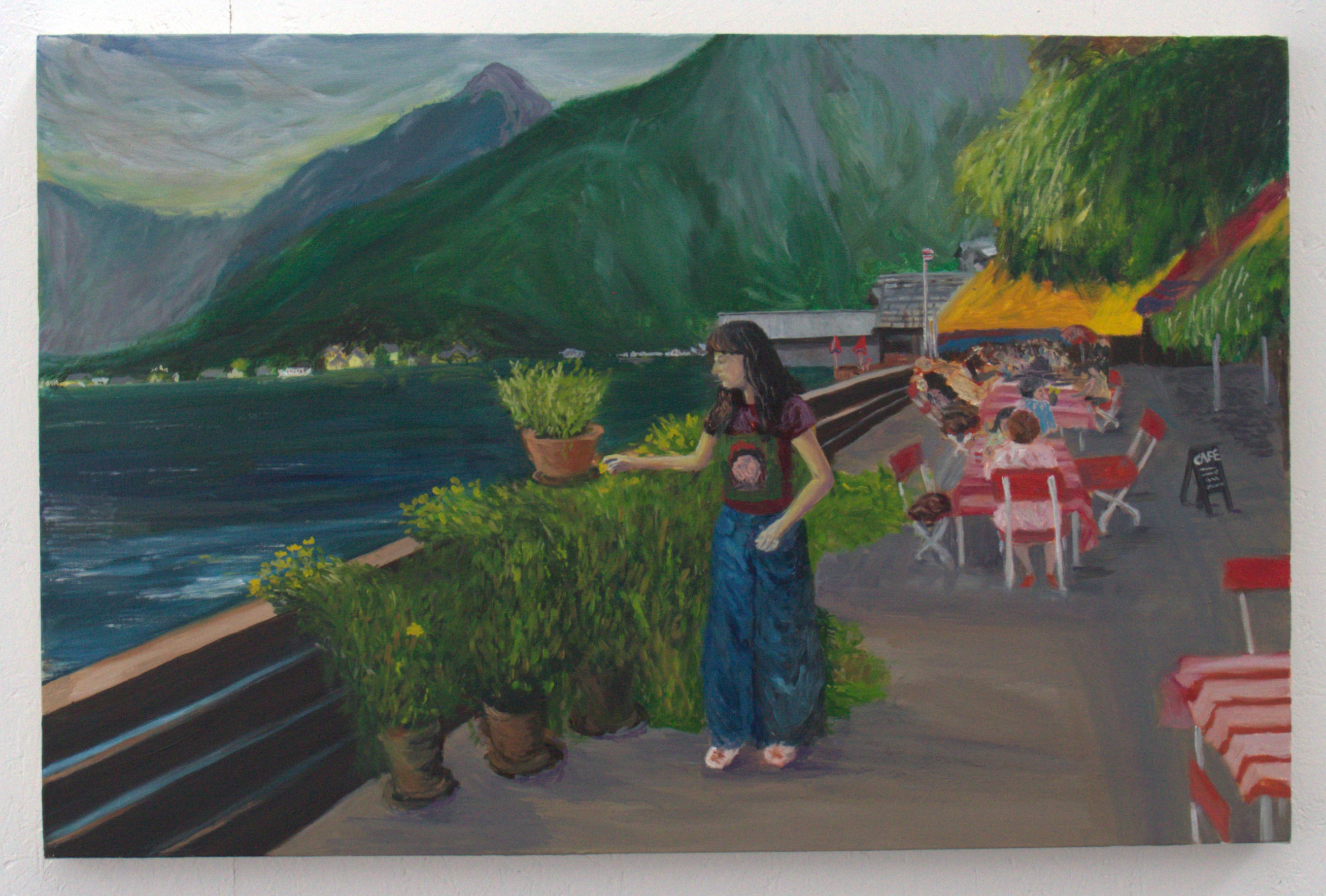 A woman wearing a black top and blue trousers stands by a railing at a lakeside promenade, holding a flower pot. In the background, tables with red and white checkered tablecloths are visible, along with green plants, mountains, and a cloudy sky.