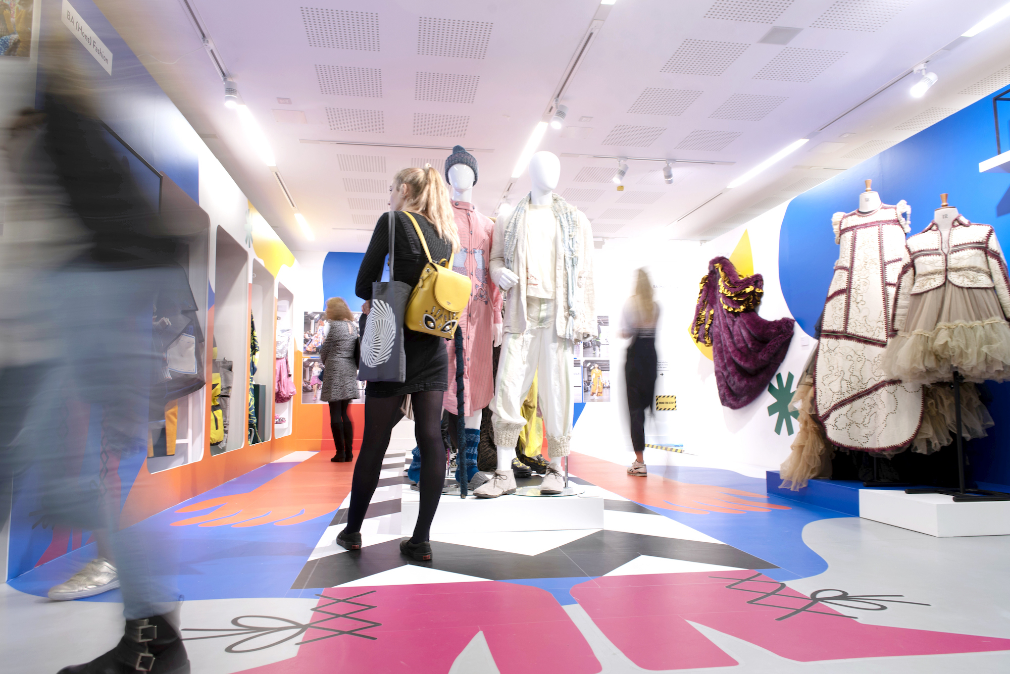 People moving around the Fashion display at the AUB Summer Shows. Various garments are on display on mannequins and on the walls.