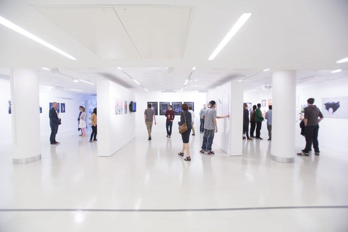 People moving around a large gallery space looking at artworks during an exhibition.