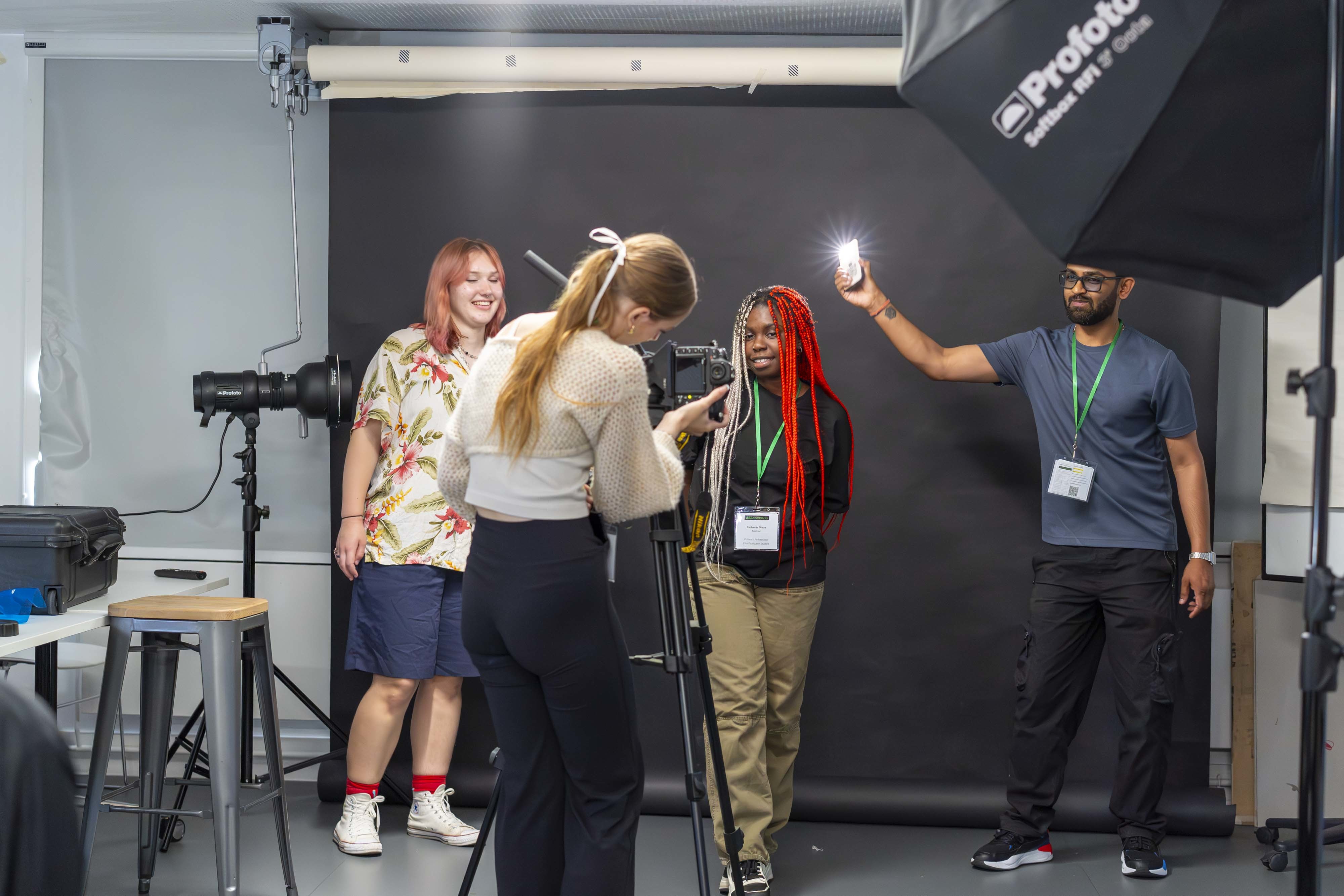 AUB Outreach Ambassadors working with a young person as they prepare to take a photo in a photography studio.