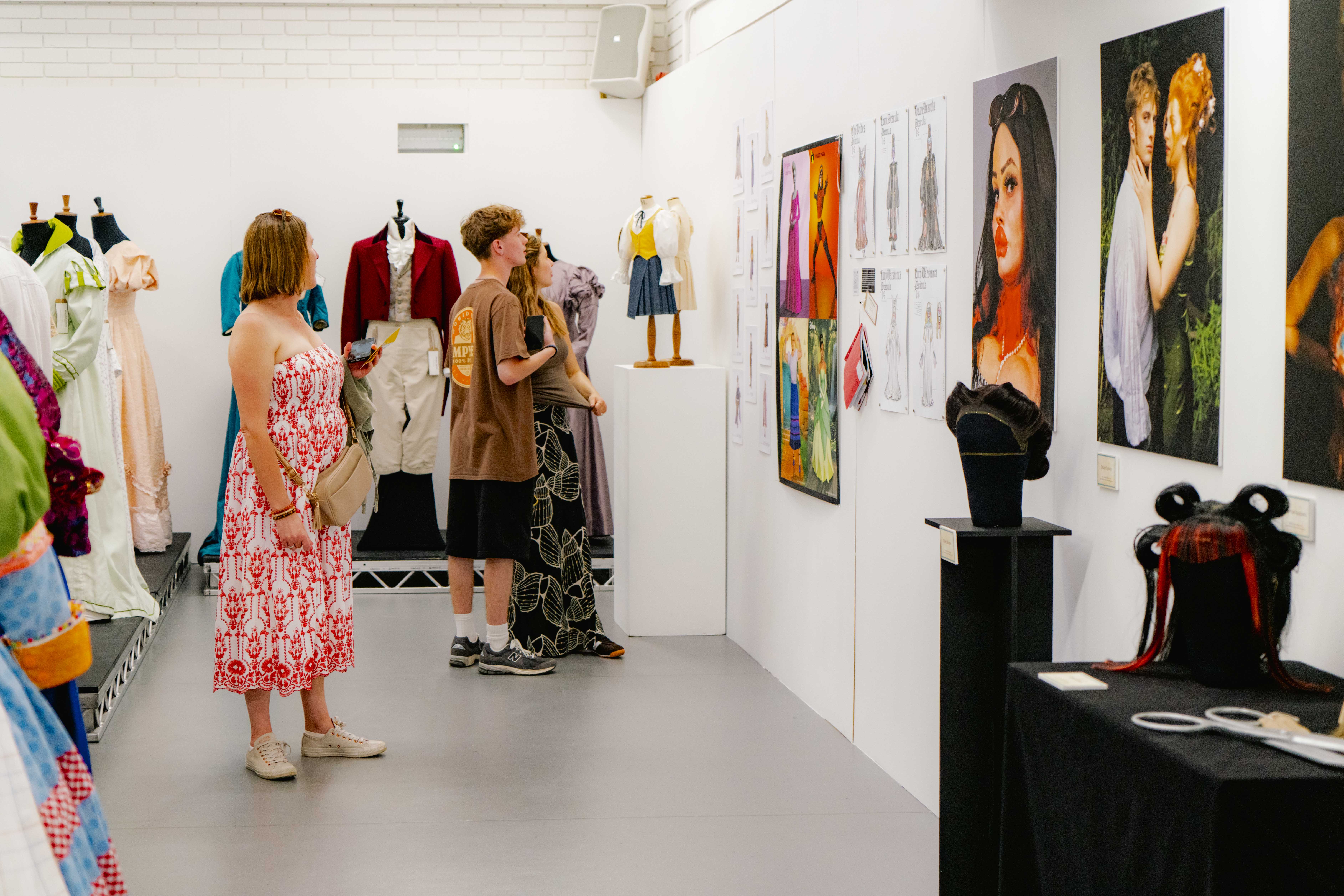 People looking at colourful artwork and costumes in a white studio.