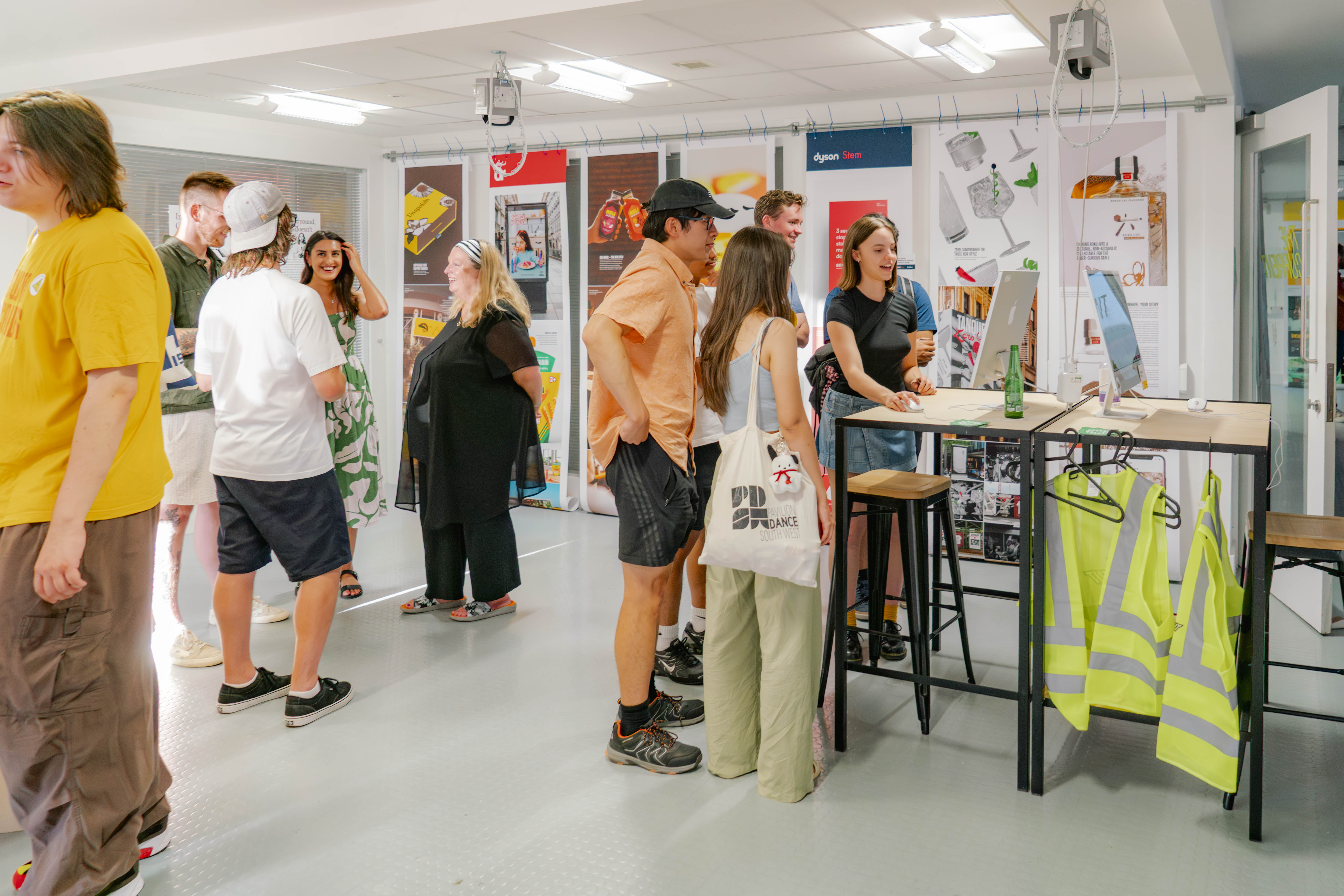 People stood talking in a graphic design studio with vibrant work hung on white walls.