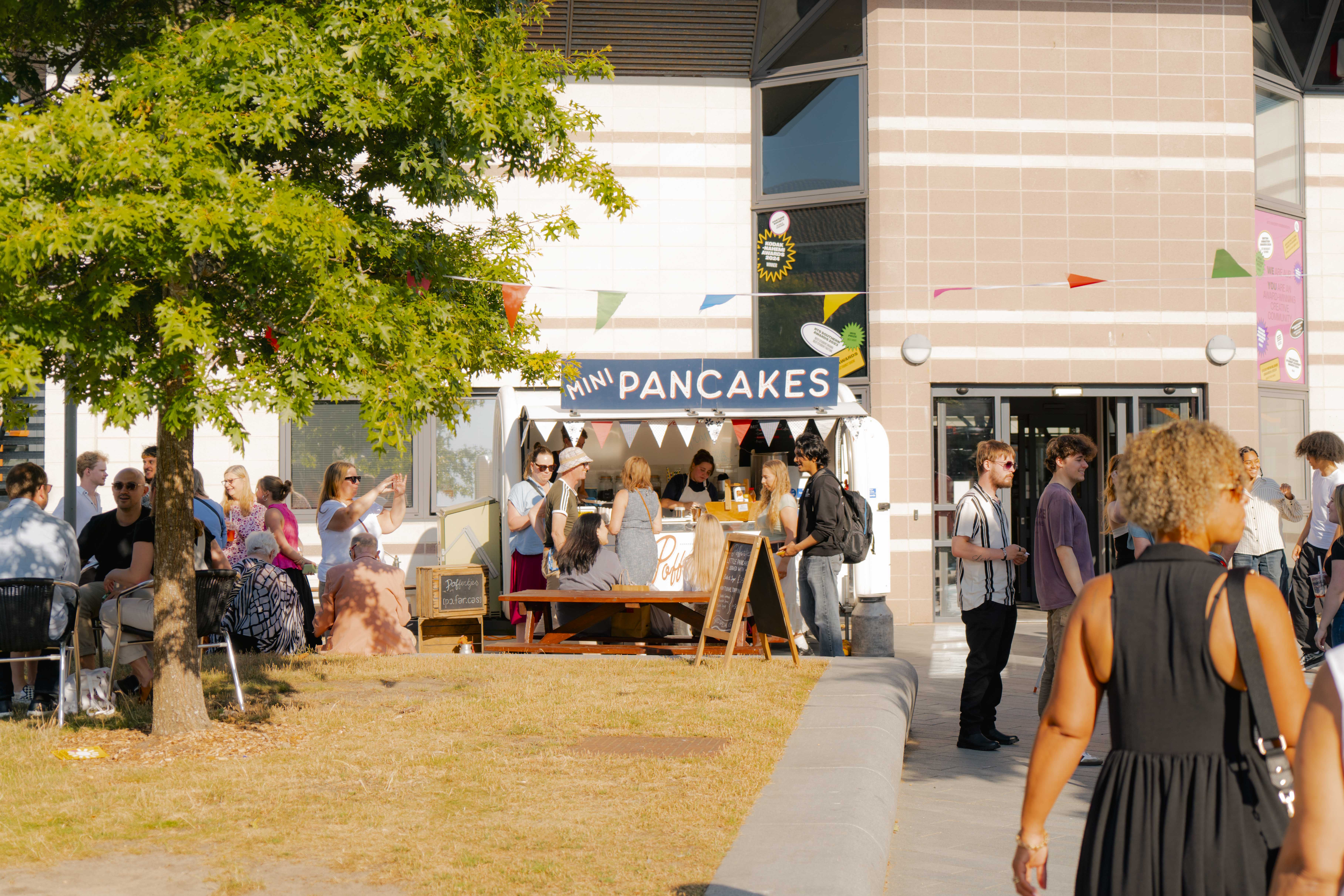 Mini pancakes stall with bunting on AUB Campus in front of the library, a busy, sunny afternoon with trees in view.