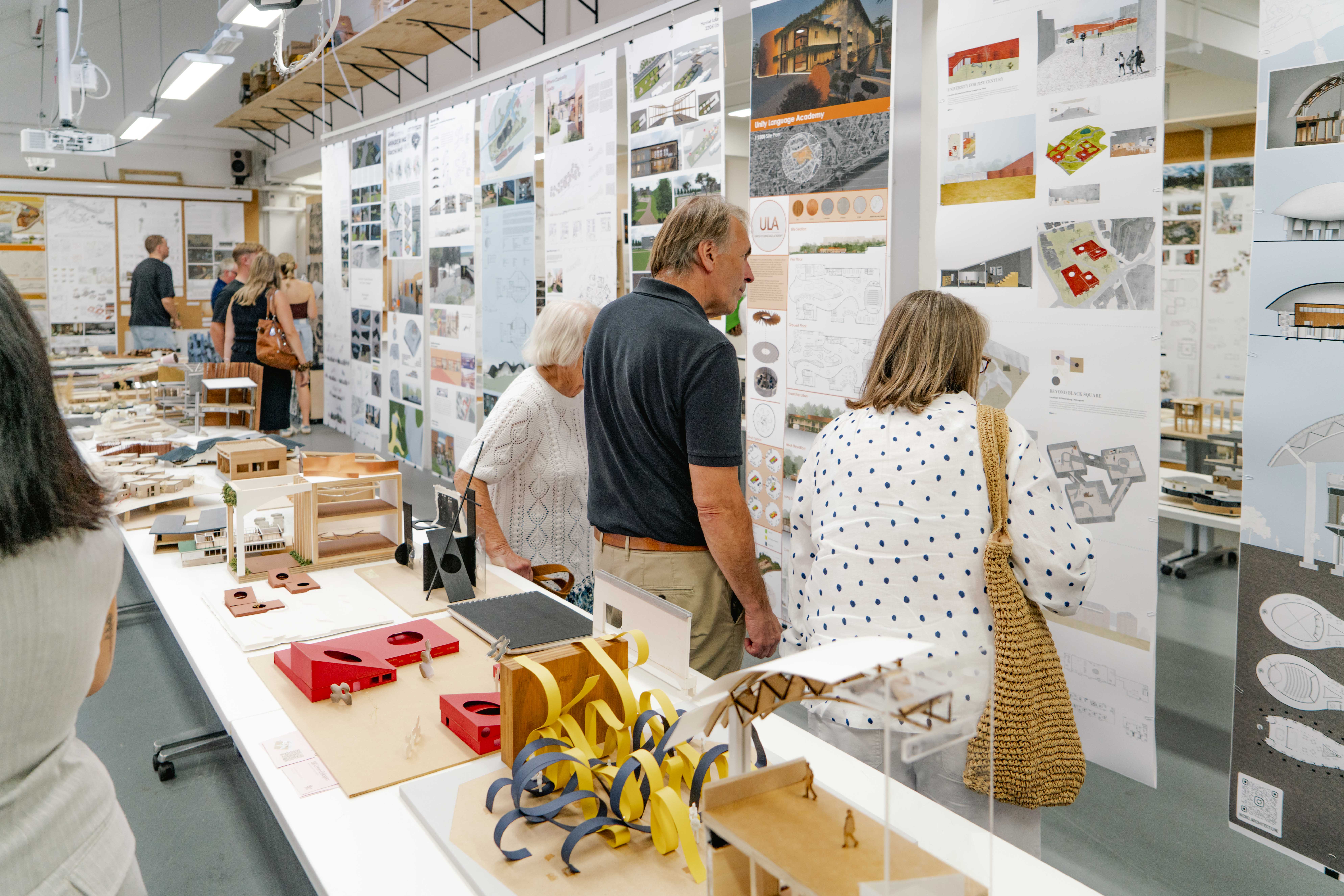 People looking at hung up architectural work, detailed table of colourful architectural models in front of them.