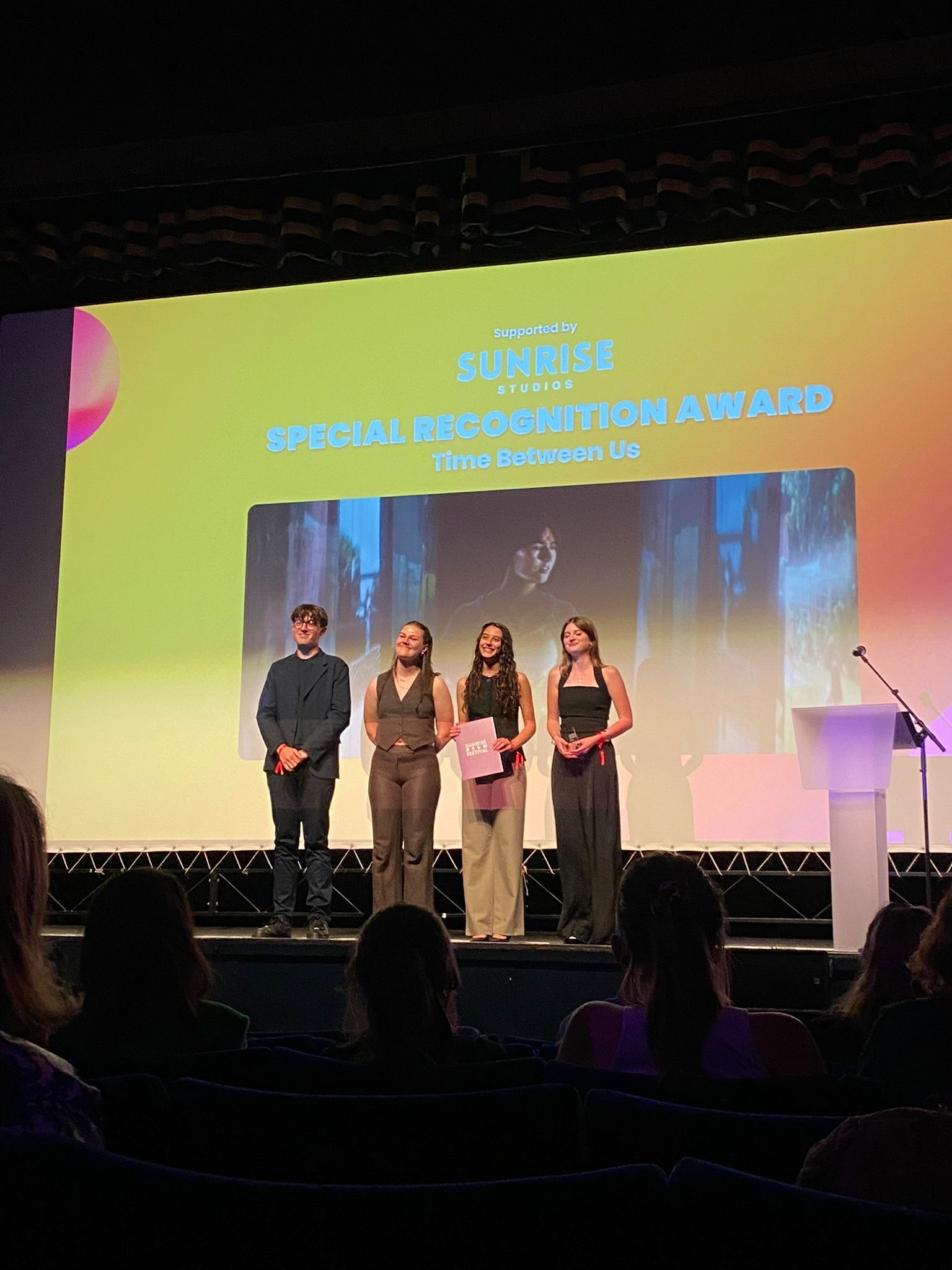 Four people on stage at awards ceremony with colourful gradient backdrop displaying "Social Responsibility Award" text and sponsor logos.