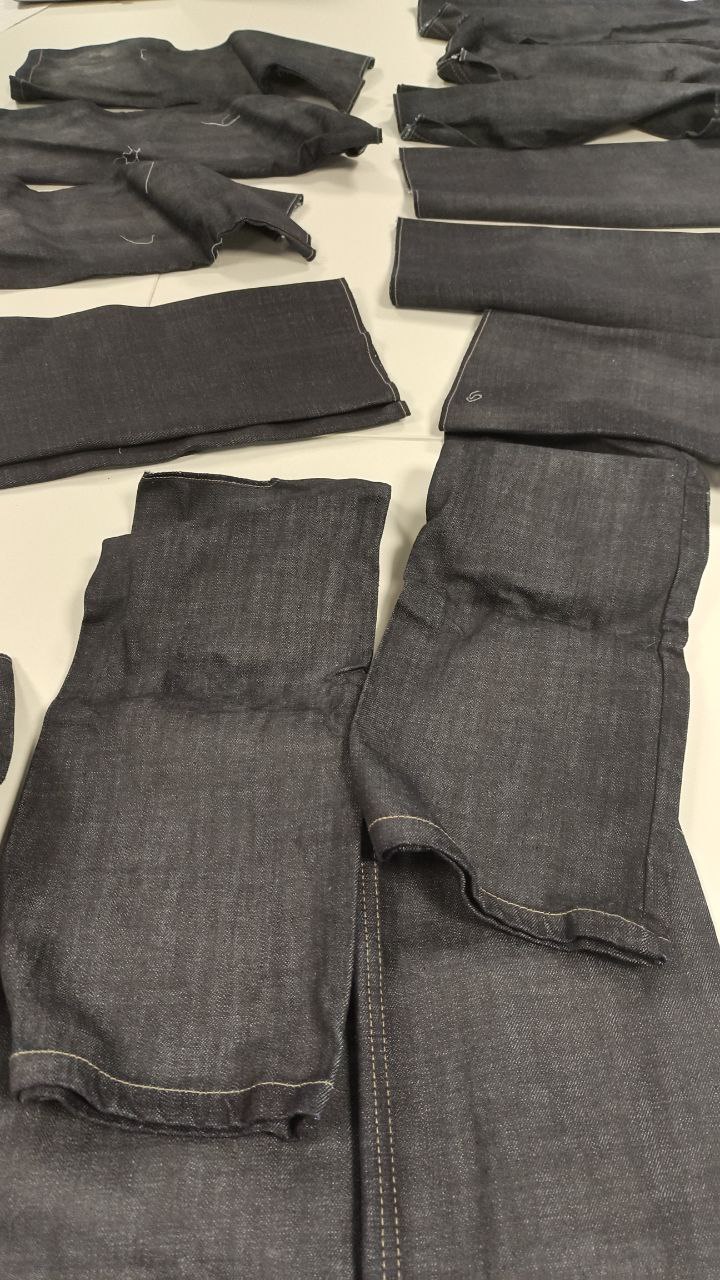 Folded dark denim jeans and trousers laid out on a light surface, with several pairs arranged in rows.