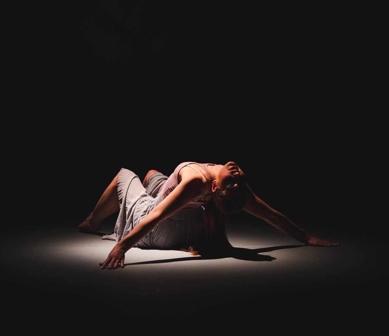 A dancer sitting onstage doing a backbend, there is a spotlight on her.