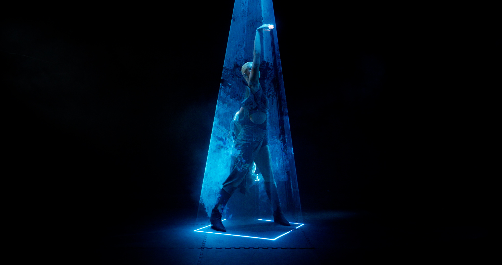 Blue translucent triangular structure illuminated from within, casting bright light onto square base against black background.