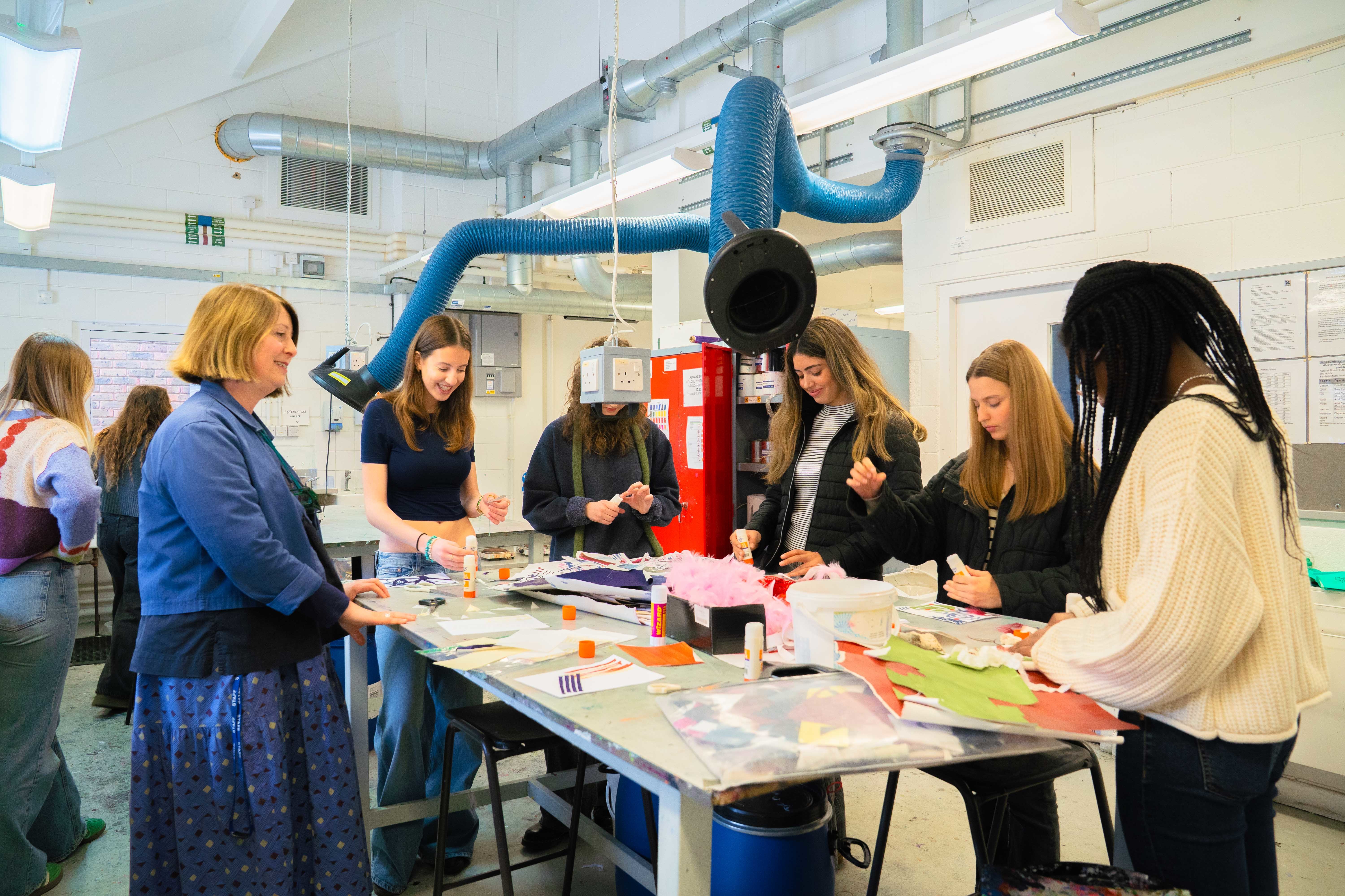 Five young people and a member of Arts University Bournemouth staff standing around a table in a studio taking part in a Textiles Design workshop.
