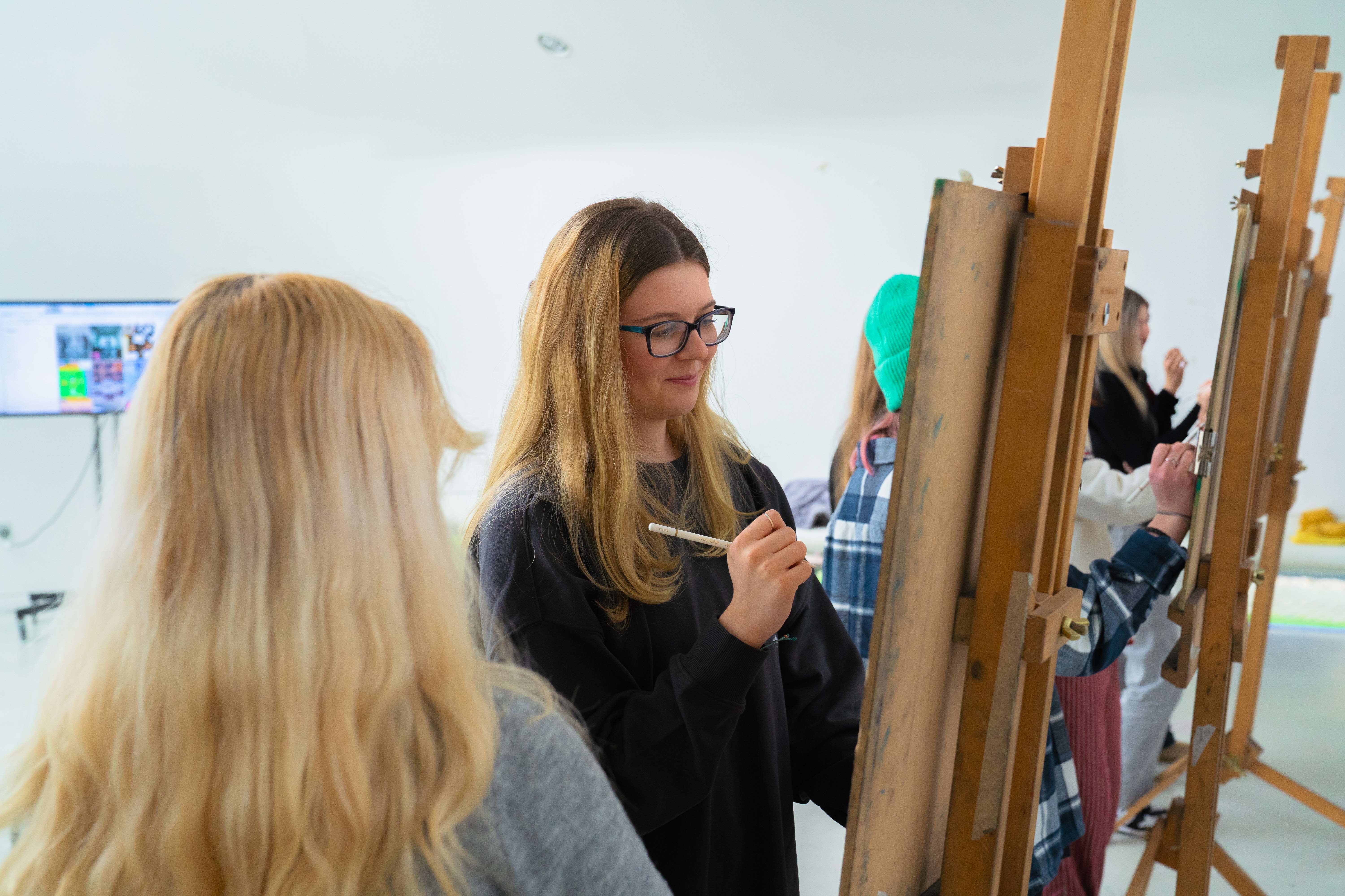 A row of young people painting on canvases on easels in a studio at Arts University Bournemouth.