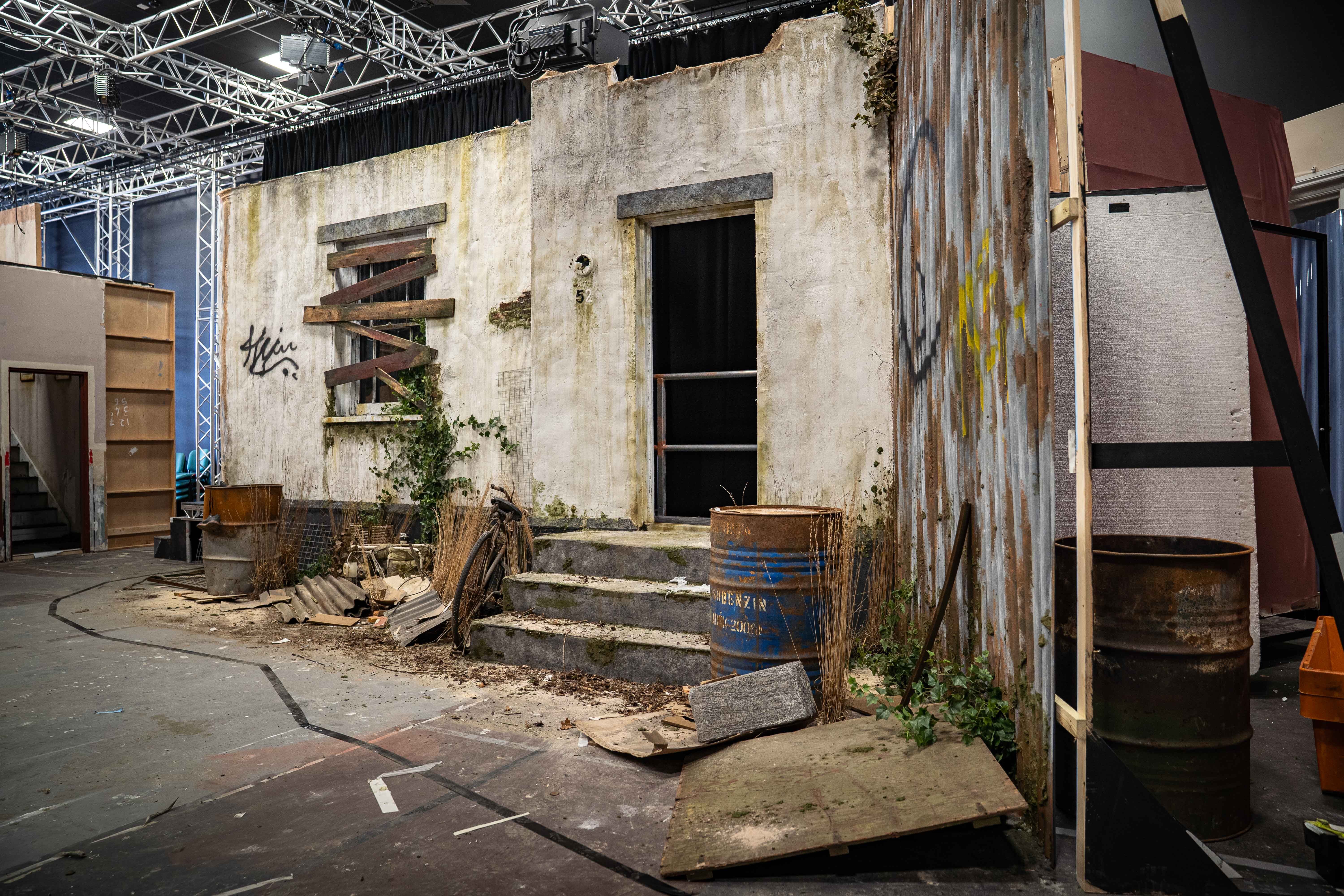 Weathered concrete structure with wooden stairs, exposed metal beams overhead, scattered debris and wooden crates on concrete floor.