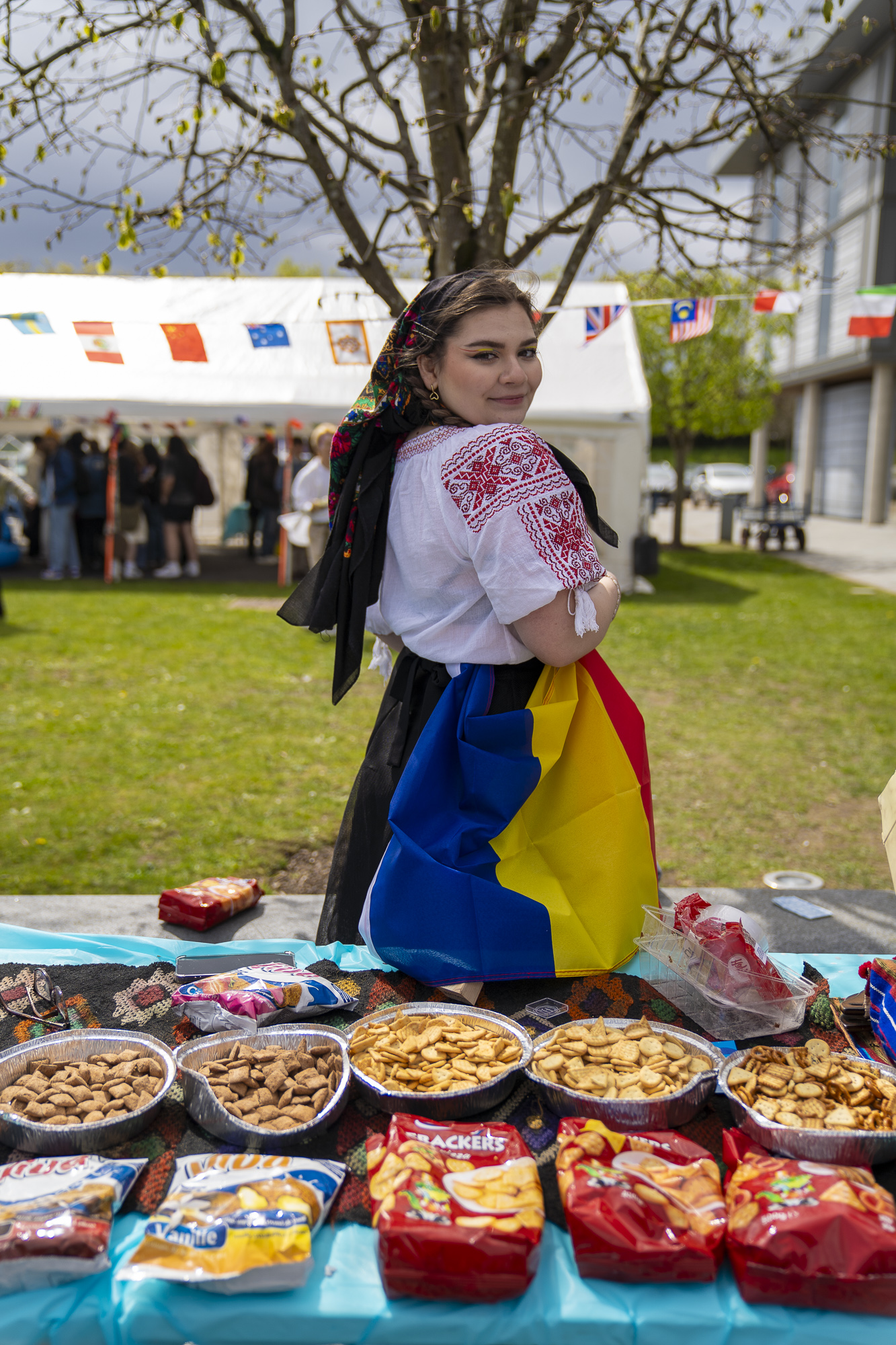 Student wearing colourful garments from their culture with intricate, red patterning. In front of them is a selection of crisps and snacks.