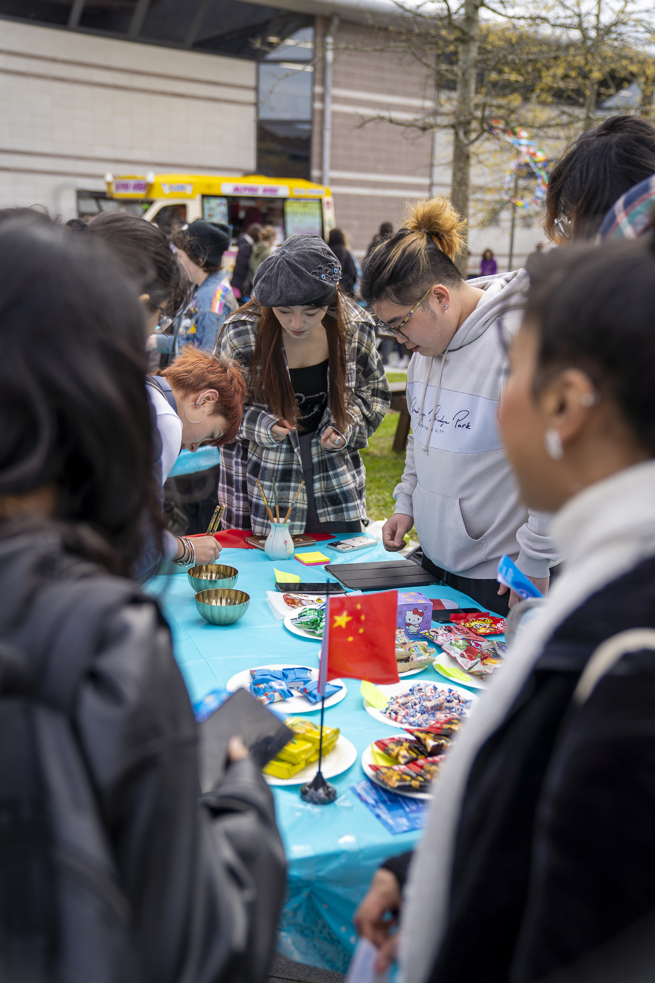 Students surrounding a blue table with a Chinese flag and snacks, outdoors at AUB Campus.