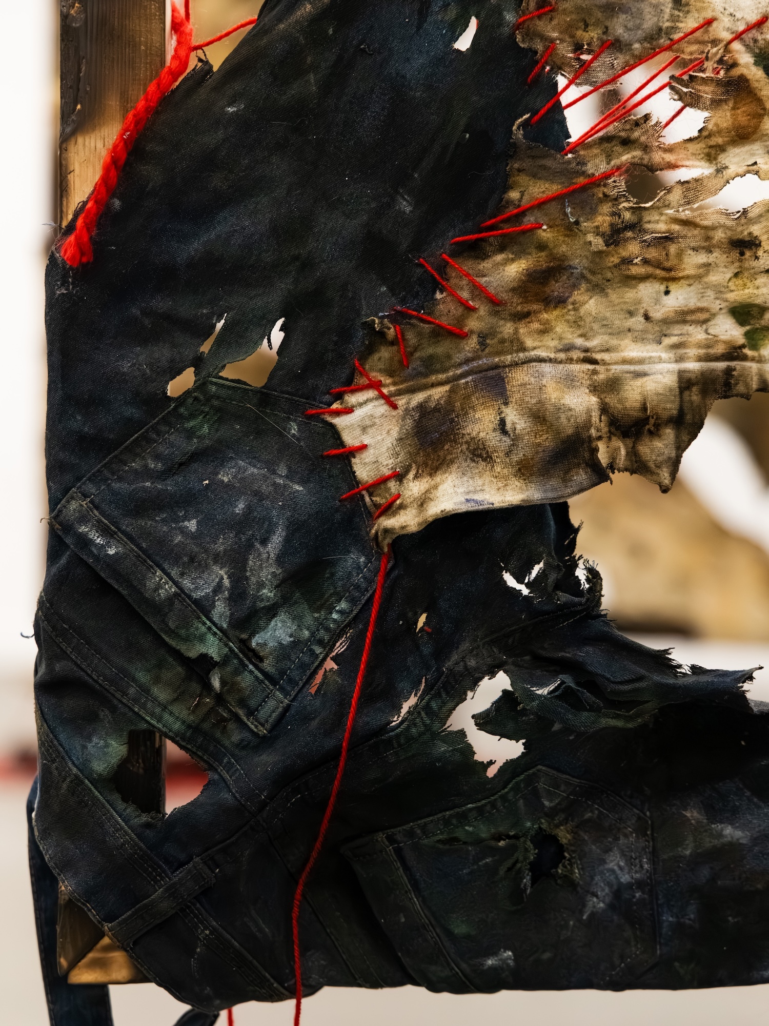 Abstract artwork with black painted areas, red linear marks, brown and beige sections, white patches, and geometric grid lines on canvas.