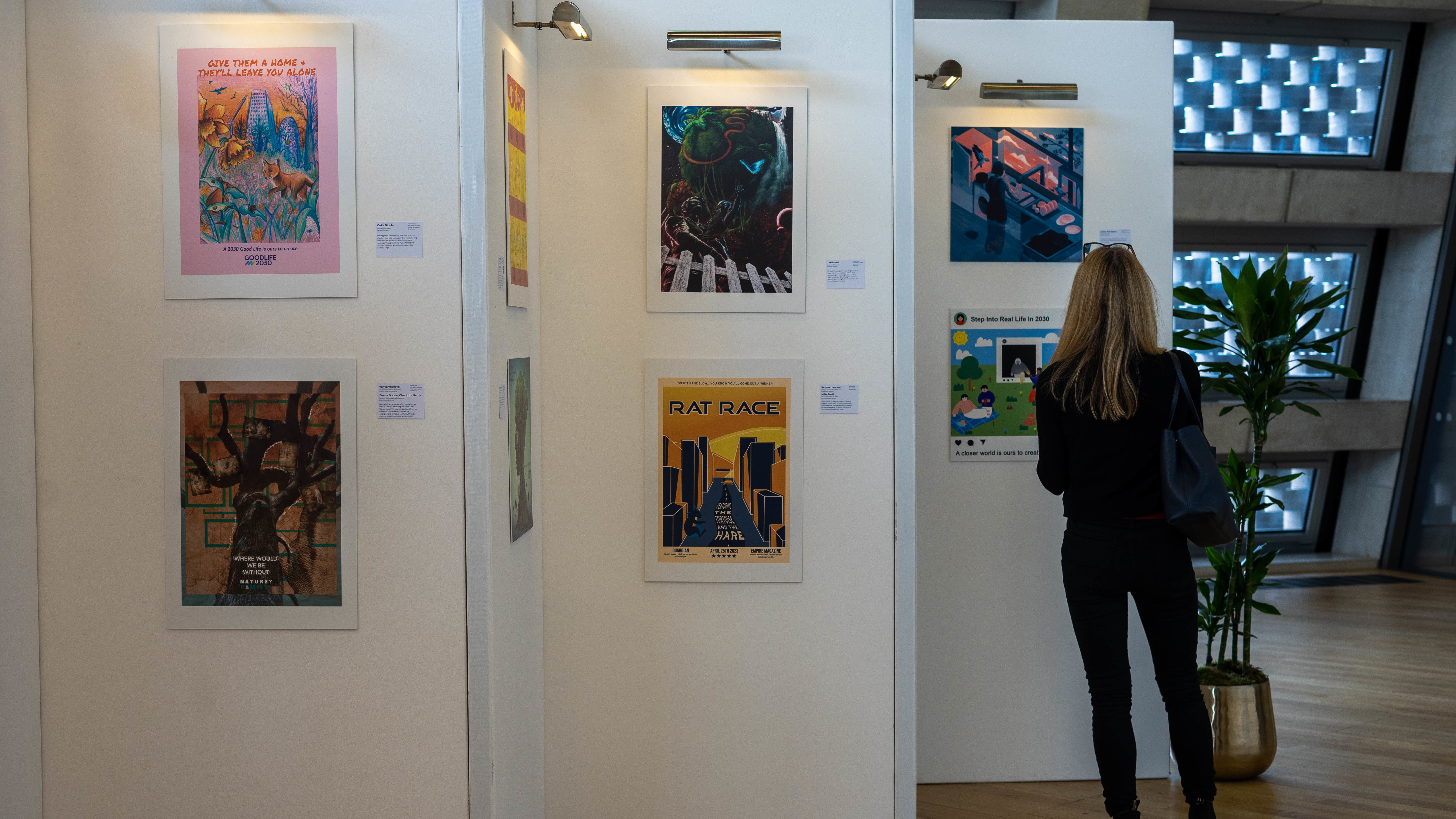 A selection of posters on a gallery wall, with a person standing to the right and looking at one.