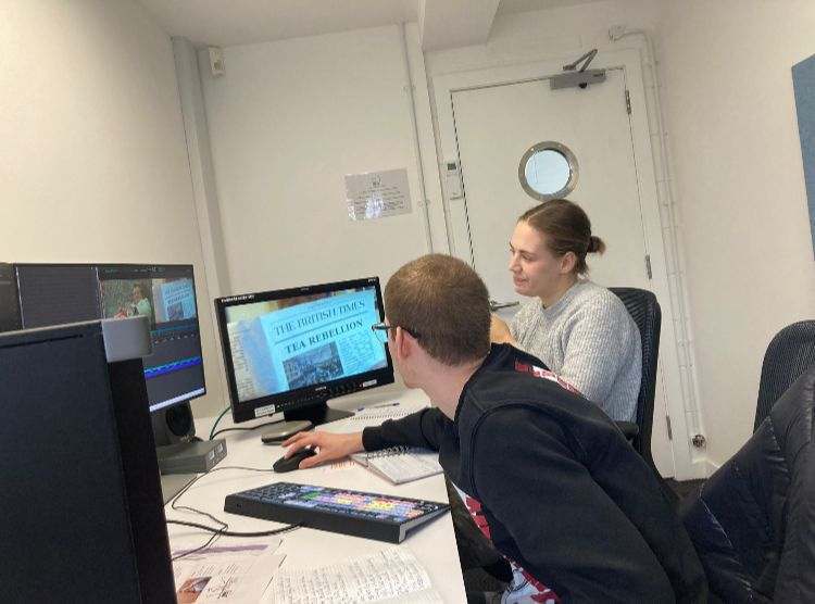 Two BA (Hons) Film Production students sat a desk in front of two monitors in an editing studio, working on the commercial 'Tea Rebellion'.