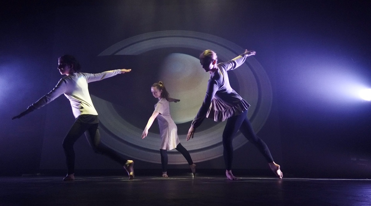 Three BA (Hons) Dance students in the middle of a performance in front of a backdrop of Saturn.