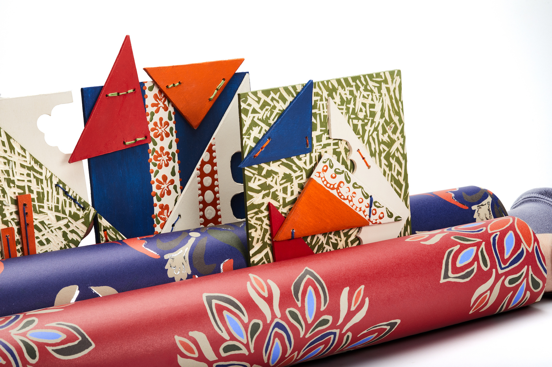 Rolls and triangular patterns of floral textiles, red, orange, green and blue, white background.