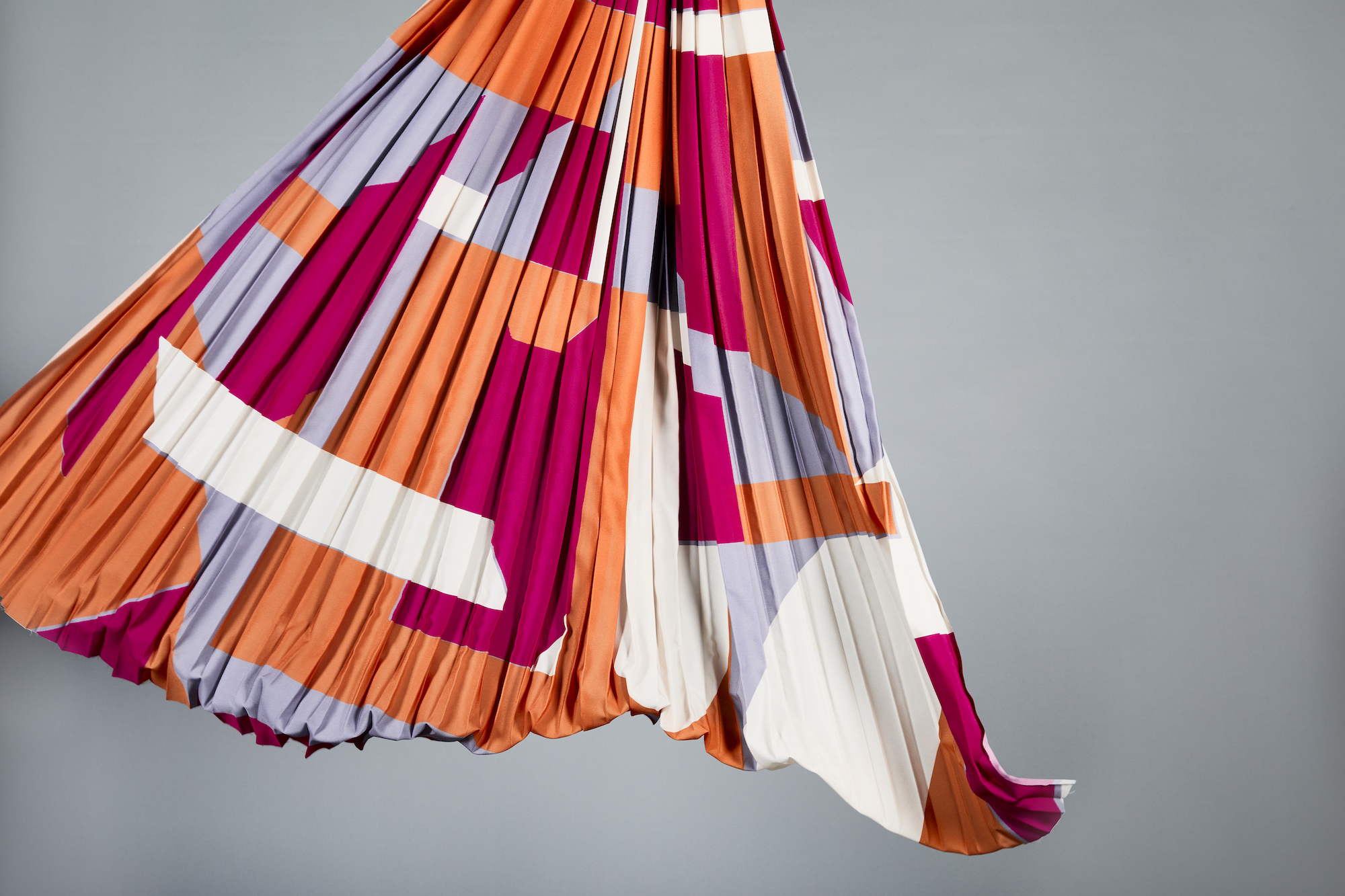 Red, orange, lilac and white ruffled textile sample, grey background.