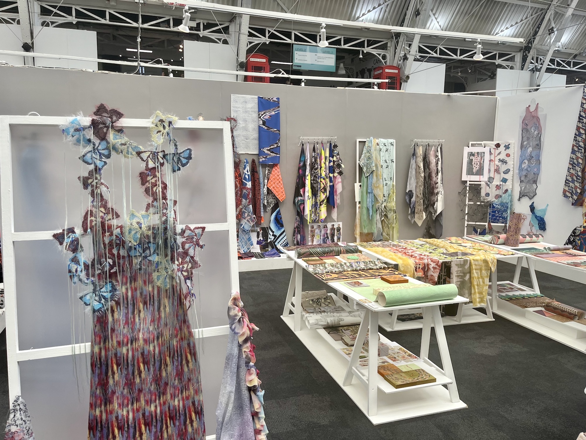 Various samples of BA (Hons) Textiles work, with a garment inspired by butterflies in the foreground,  on display at New Designers 2024 in London.