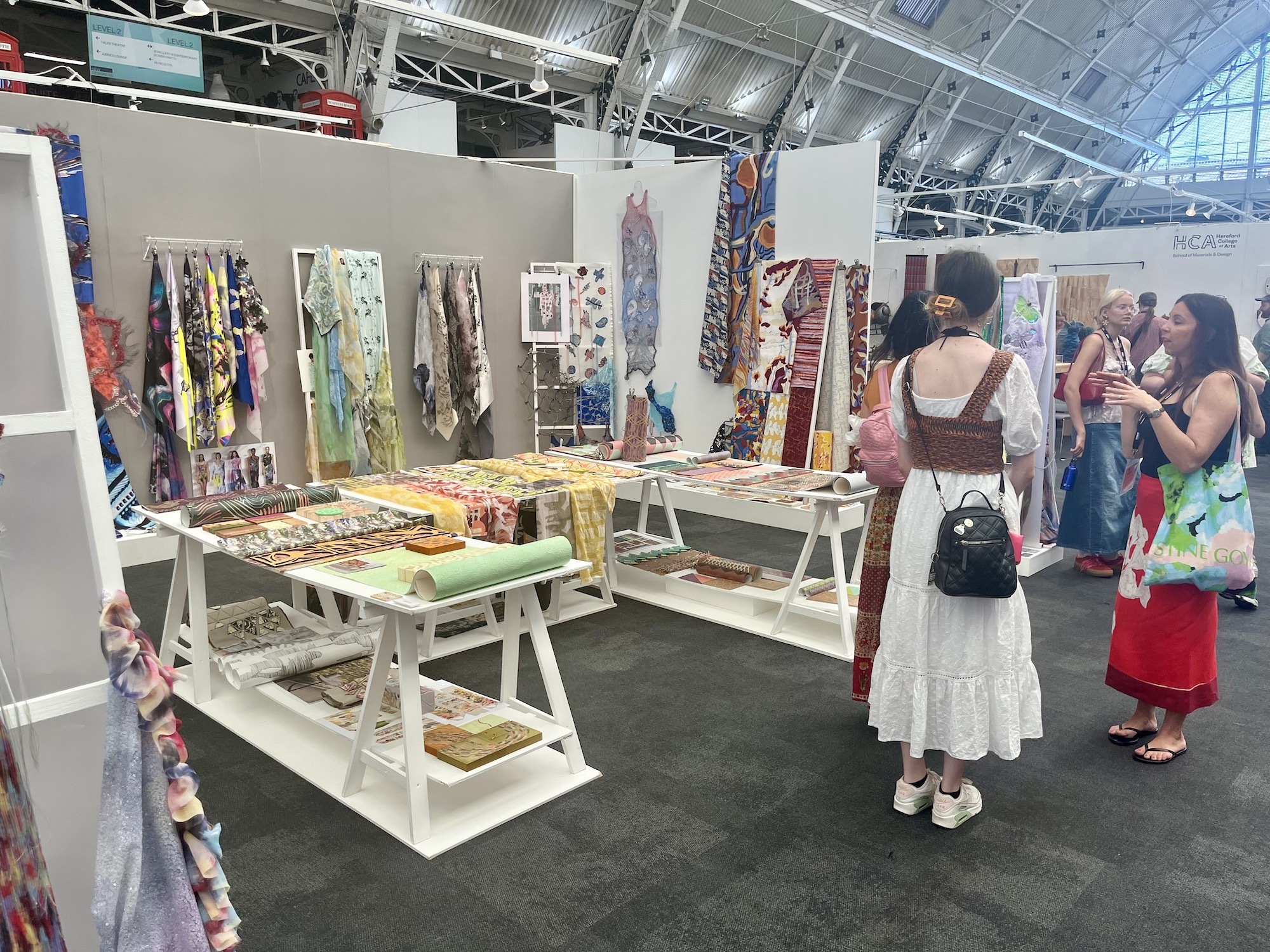 The BA (Hons) Textiles stand at the 2024 New Designers event, with various samples of work on display and people looking.