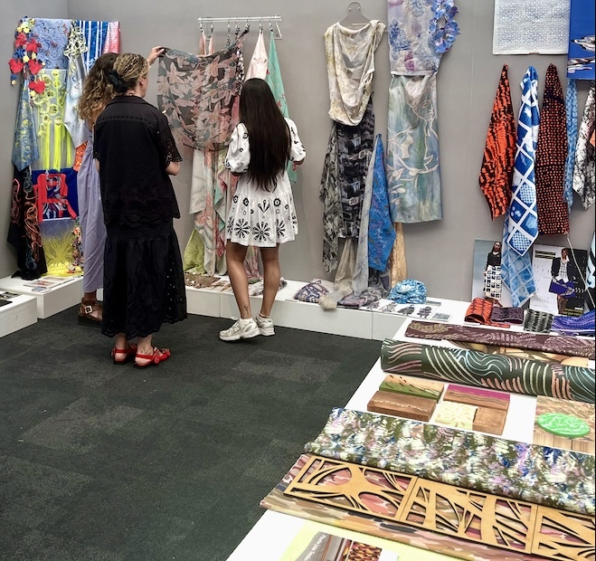 Three people examining samples of BA (Hons) Textiles work at the 2024 New Designers event.