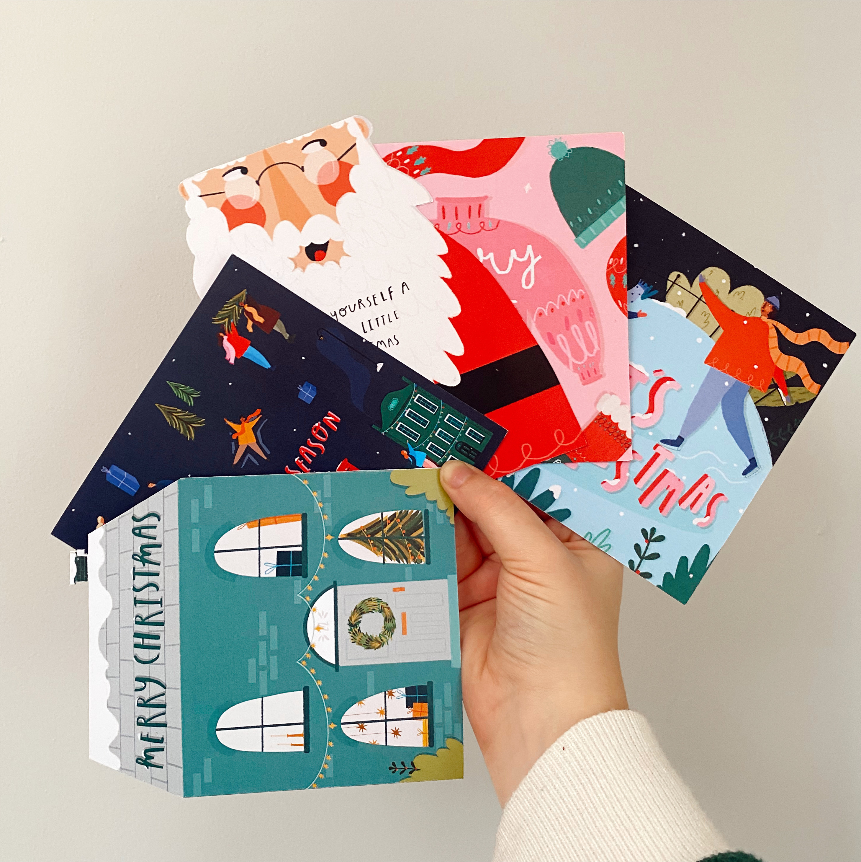 A hand holding out a selection of illustrated Christmas cards