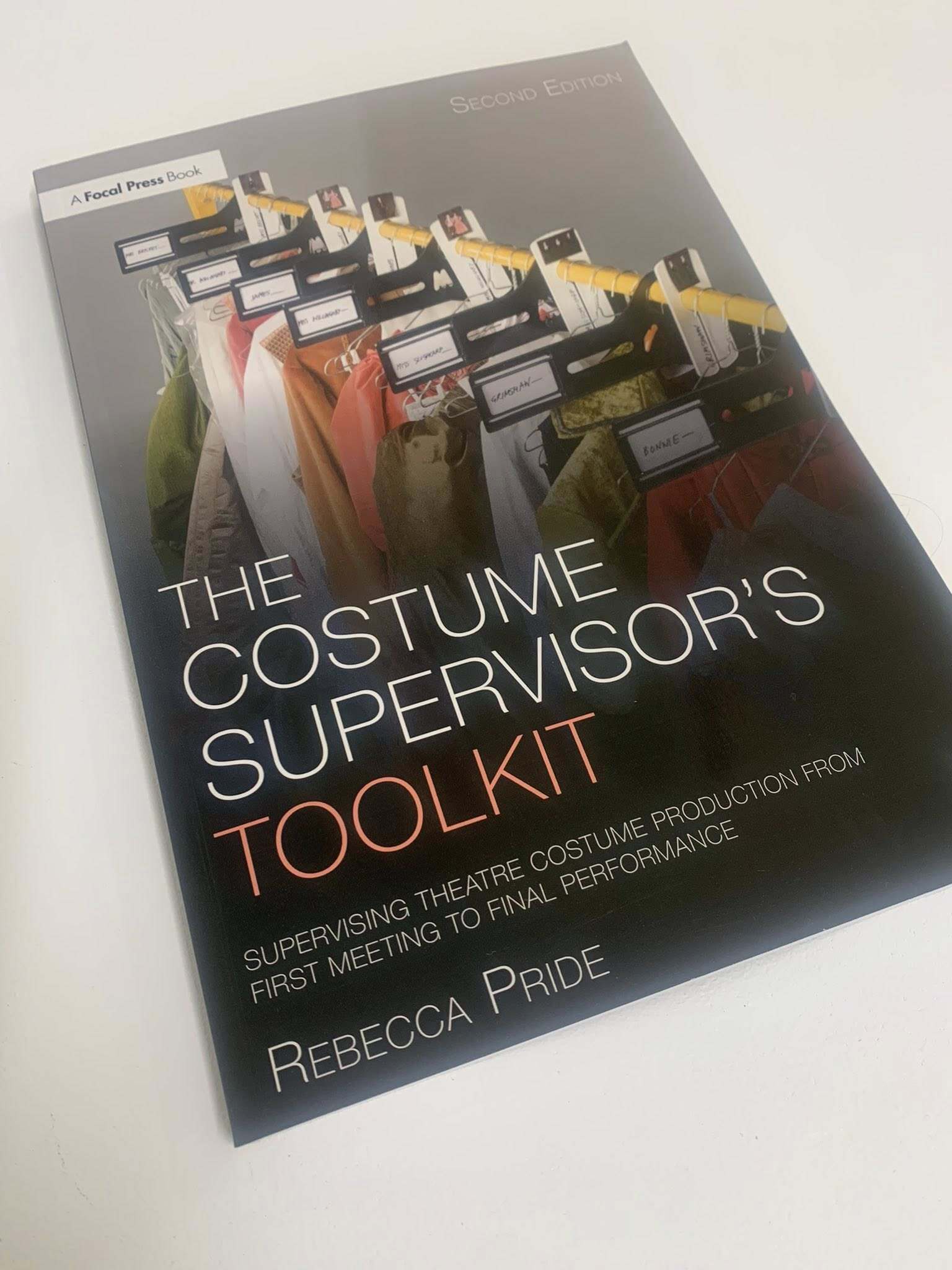 Book cover showing "The Costume Supervisor's Toolkit" by Rebecca Pride with fabric samples and theatre costume images in background.