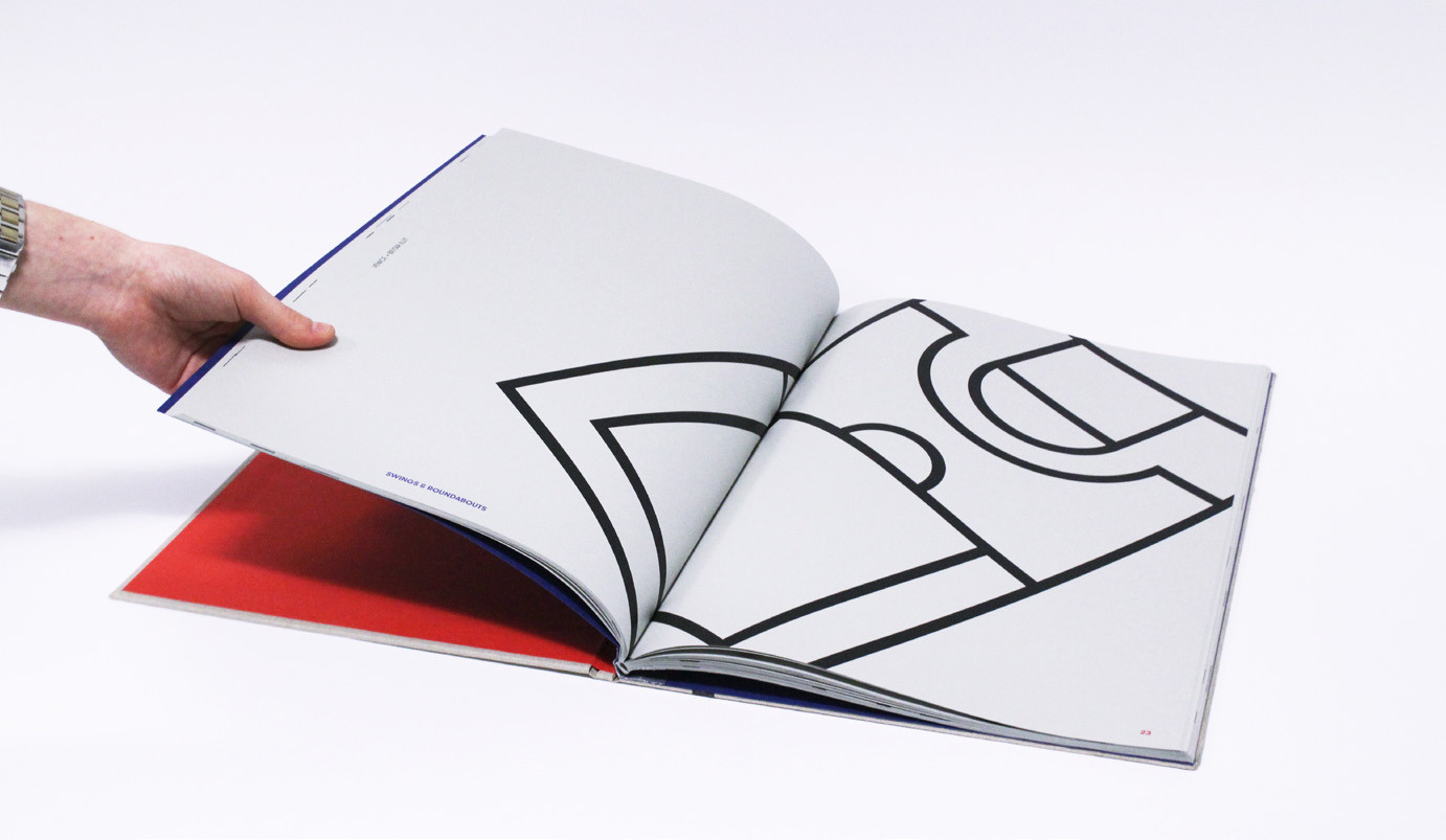A hand opens a book to a double-page spread with an abstract shape on it, made up of thick lines.