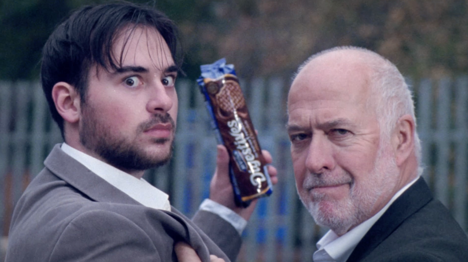 Still from BA (Hons) Film Production student commercial "The Real Deal", showing two men looking at the camera while holding a packet of McVitie's biscuits.