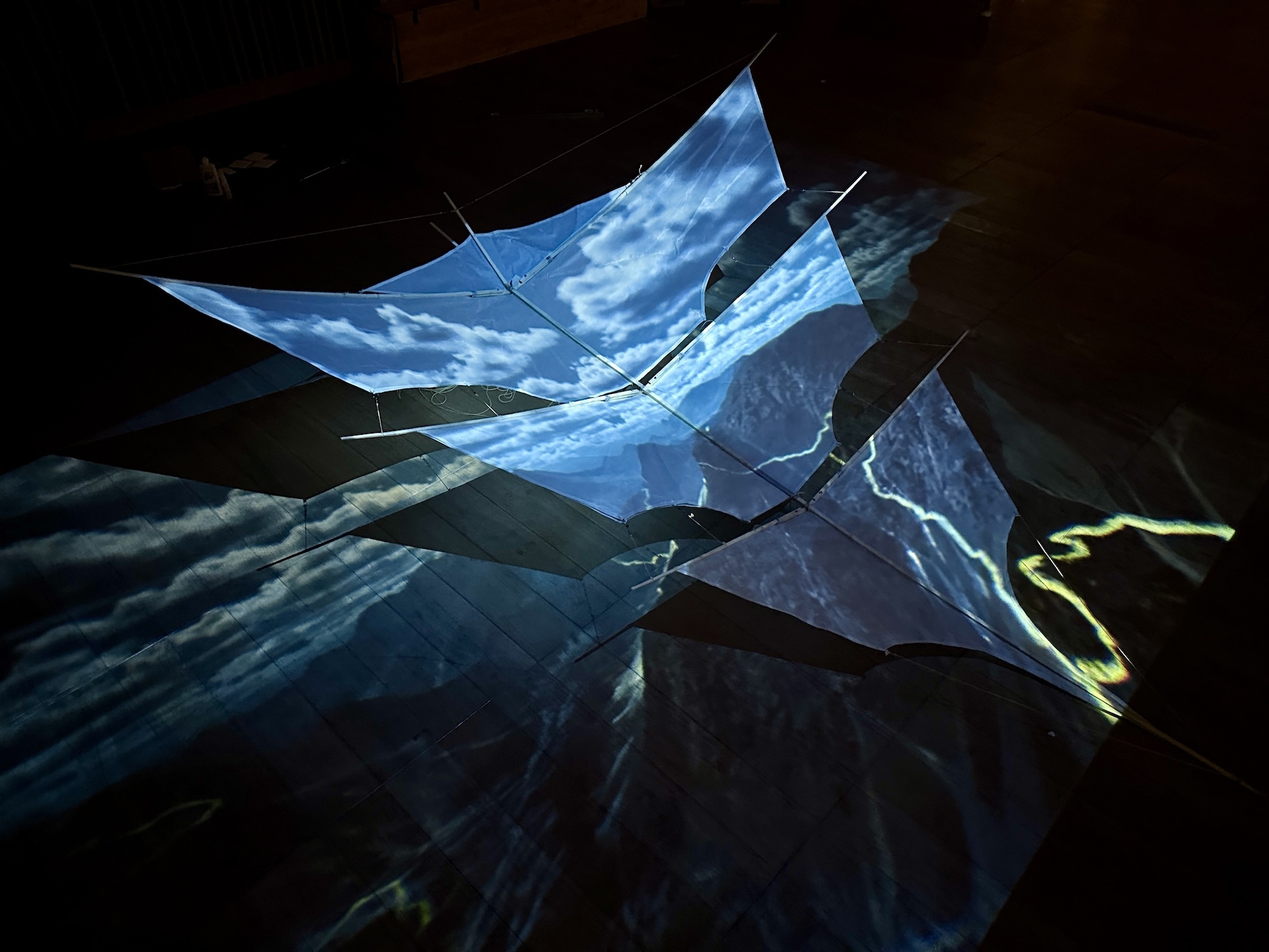 Angular blue geometric shapes with cloud-like patterns projected against dark background, creating layered translucent surfaces.