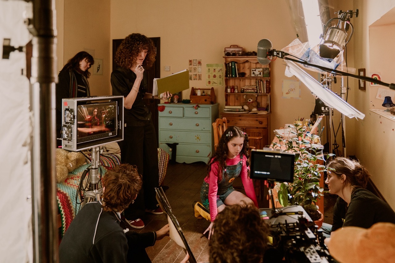 BTS shot from 'The Greenhouse Next Door' showing the film crew and actress in a bedroom.