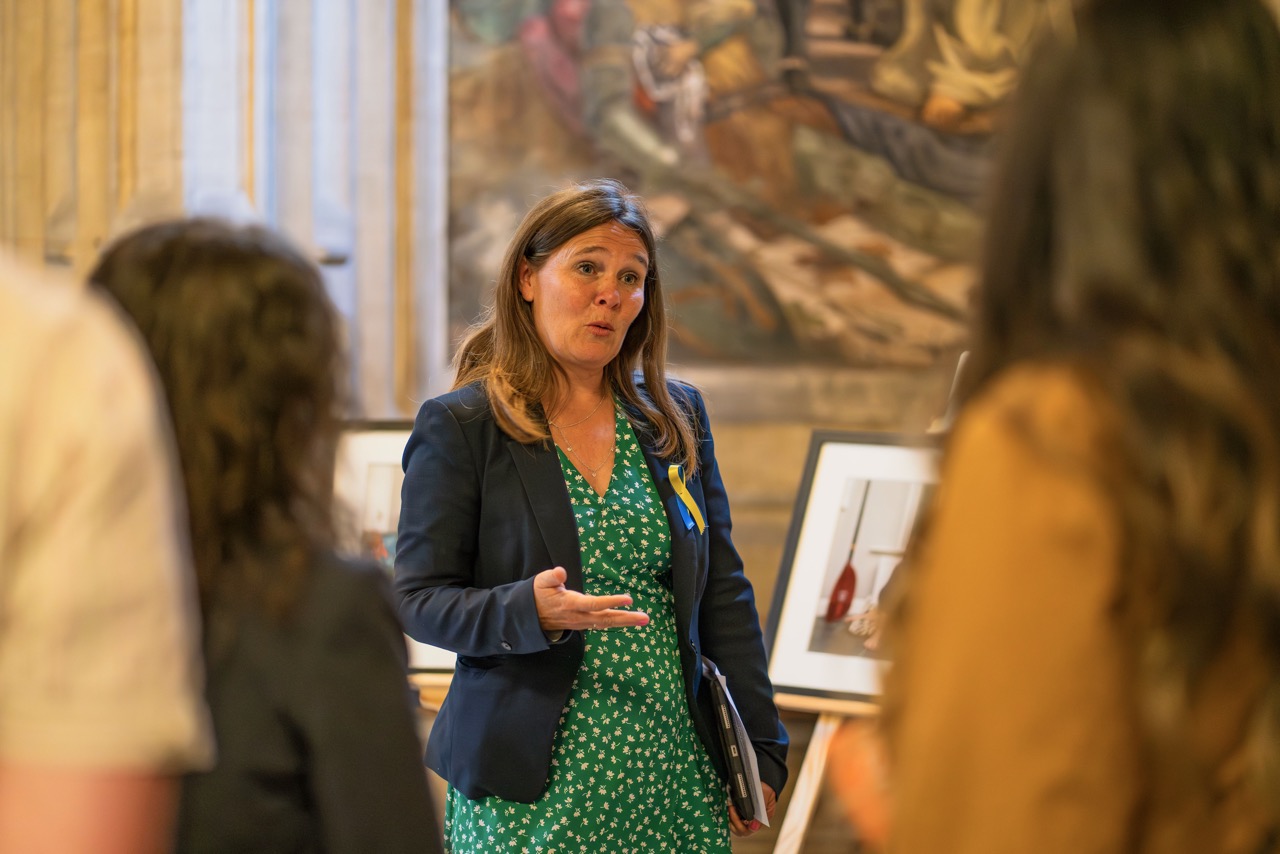 Woman wearing a blue blazer and green dress presenting to people, blurred in front.