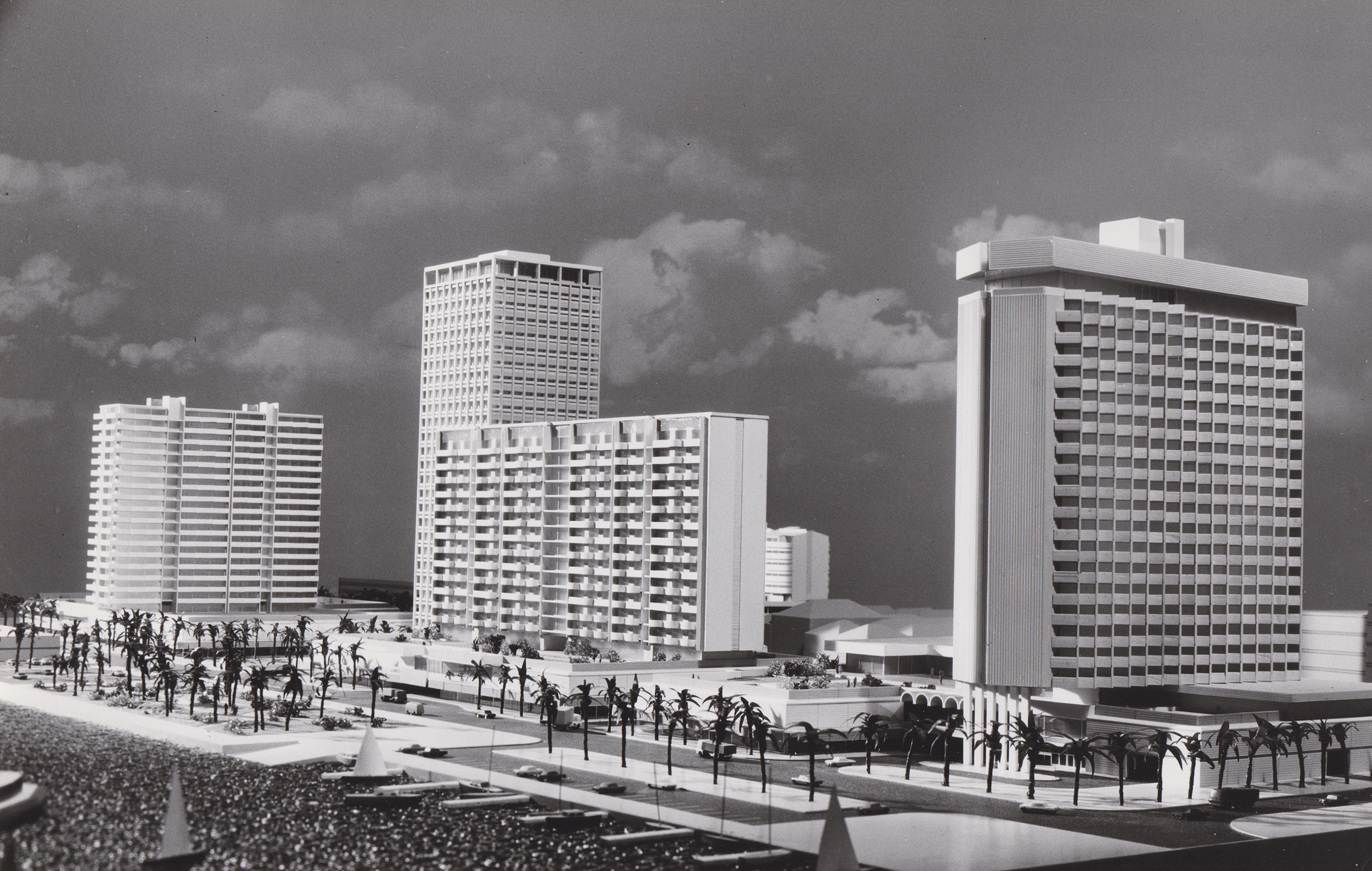 Model of four large apartment blocks with car parking and several palm trees at the bottom.