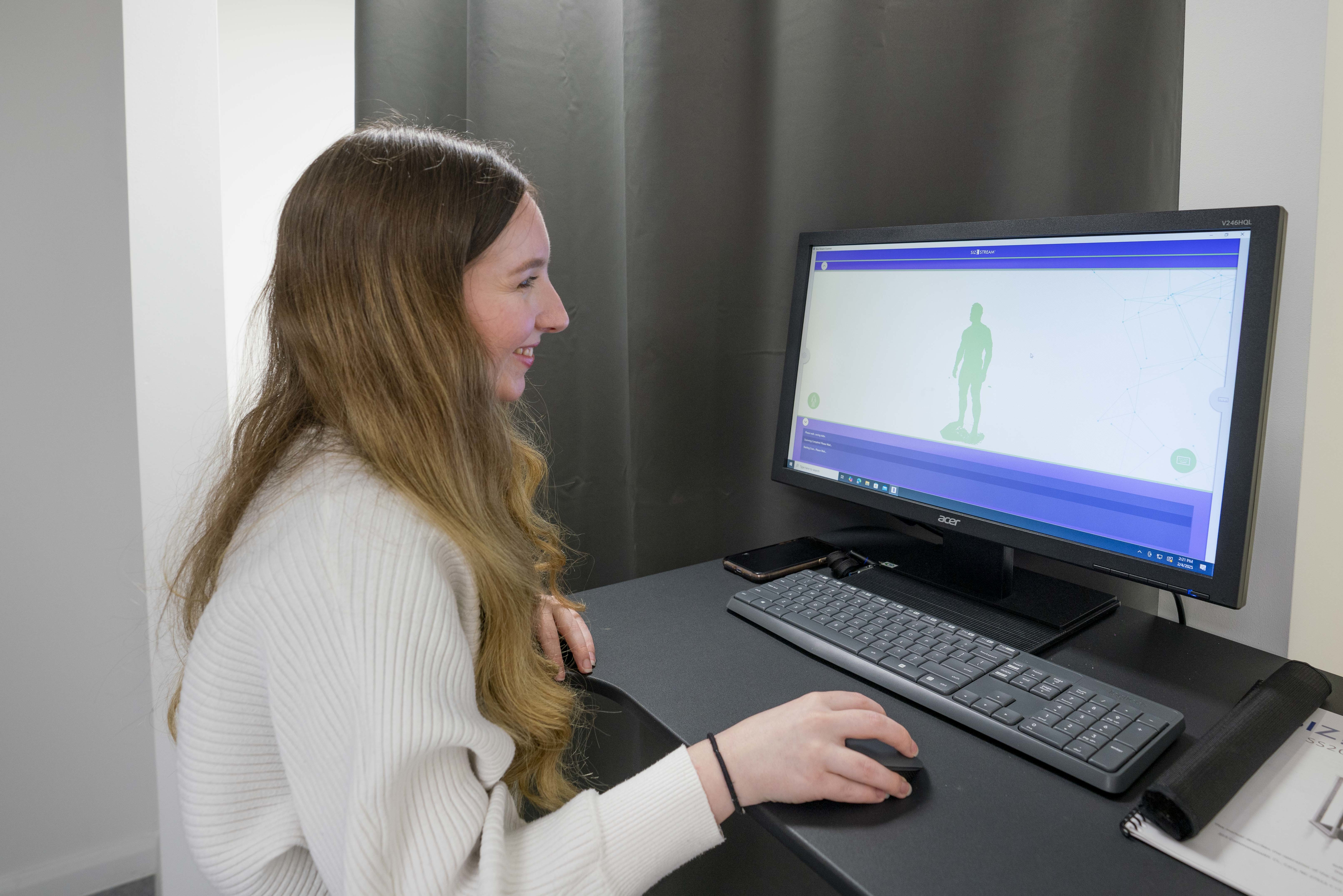 K Gibson, KTP Associate Digital Developer, viewed from the side, standing at a computer working on 3D Body Scanning software.